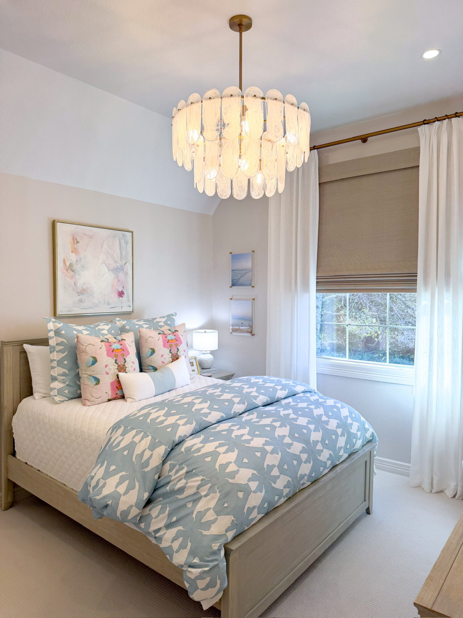 Bedroom with bed, pillows, artwork, window with curtains, and chandelier ceiling light.