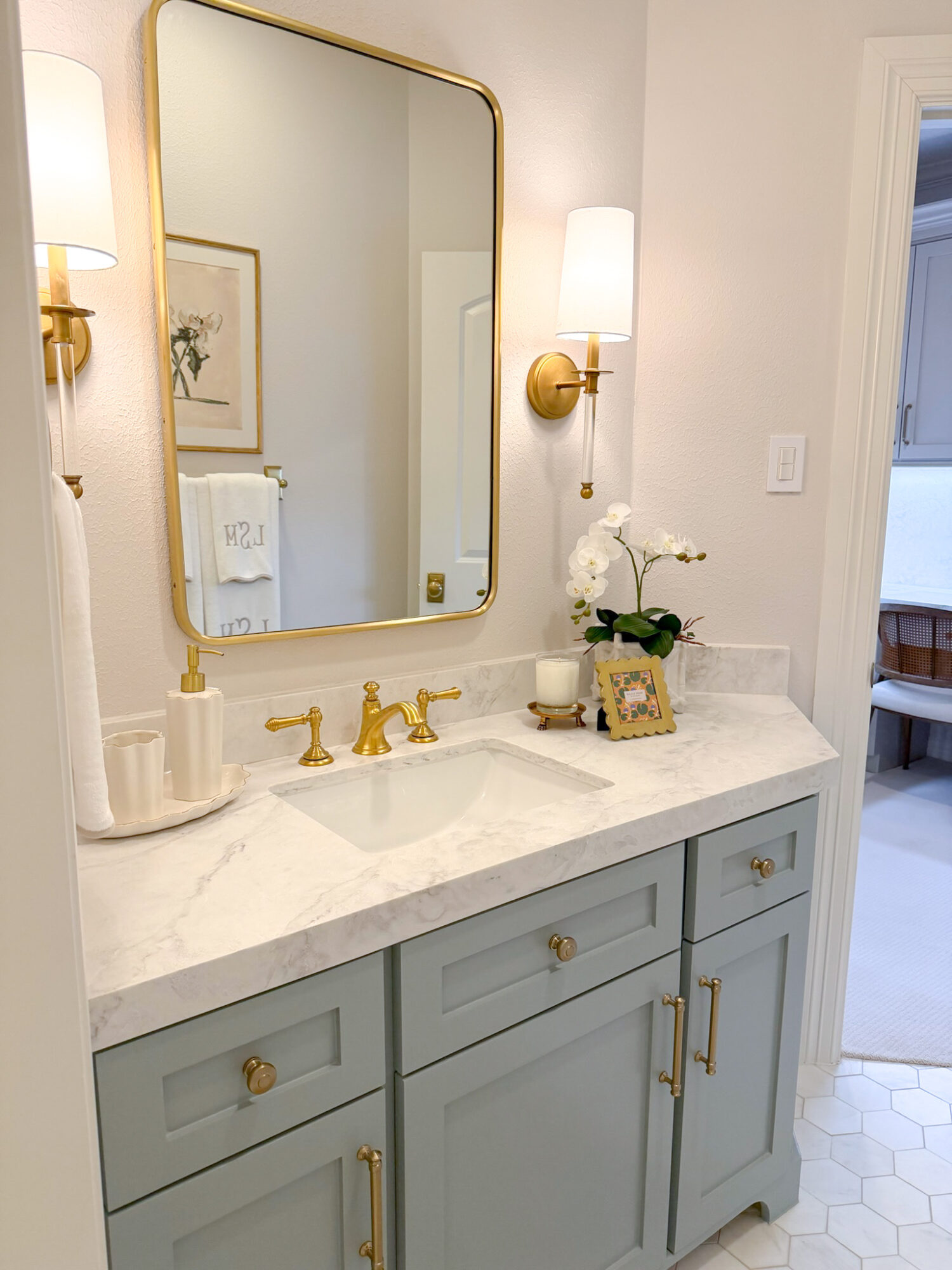 Bathroom vanity with a mirror, two wall sconces, a white marble countertop, and a potted orchid plant.