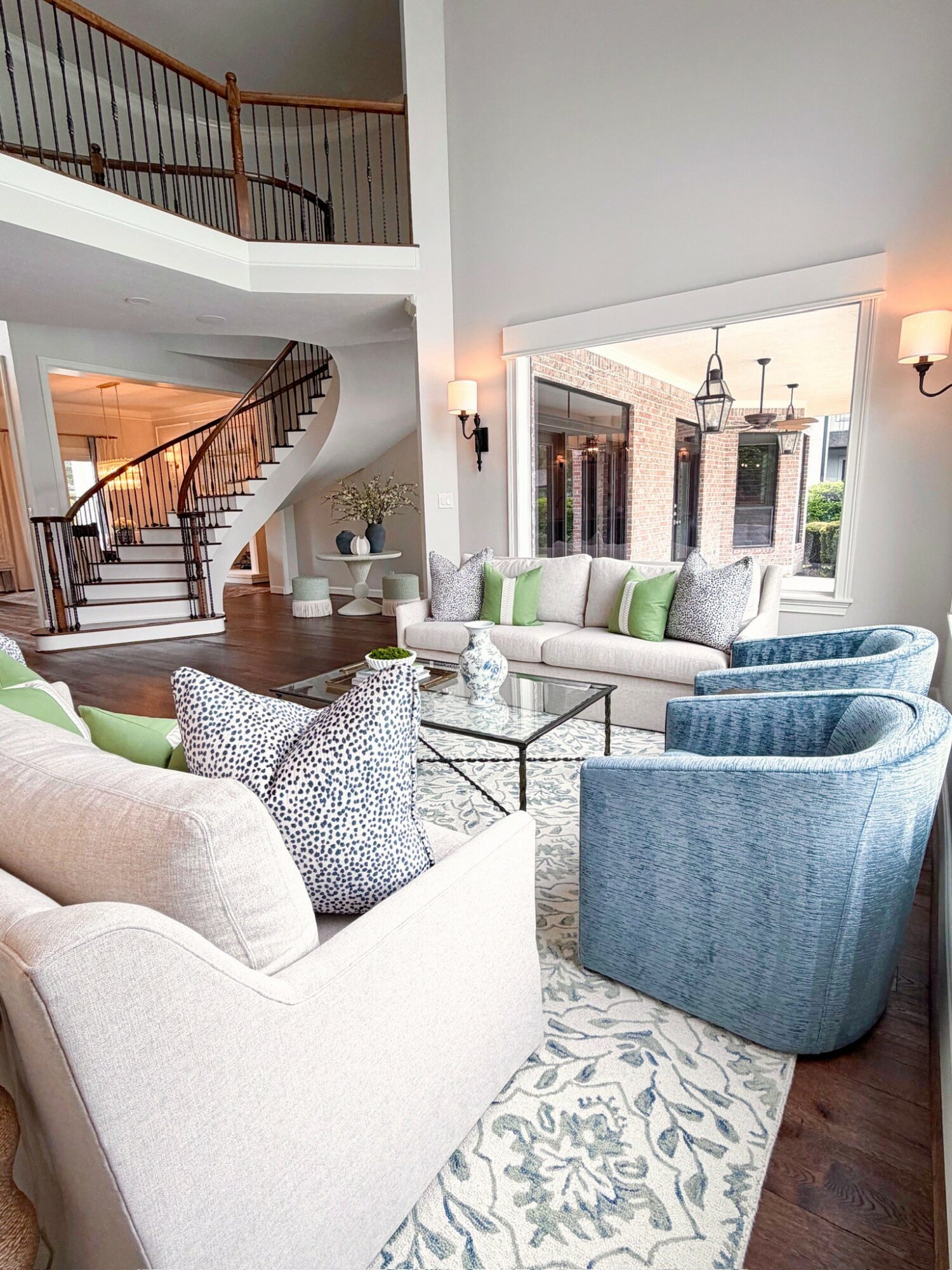 Living room with white sofa, blue armchairs, glass coffee table, and large window with outdoor view.