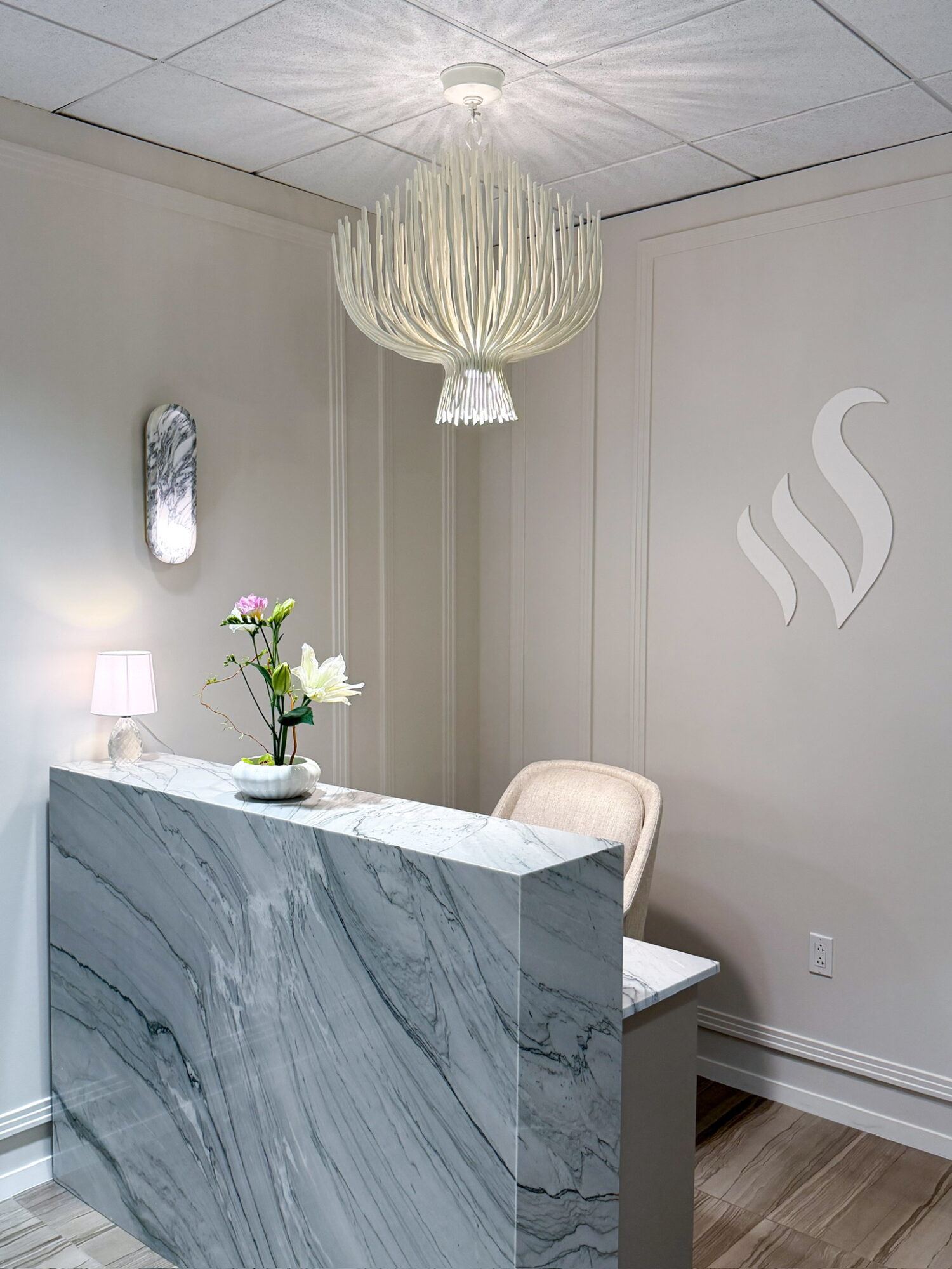 Interior space with a marble counter, a chair, a wall mirror, a lamp, and a hanging chandelier, with a steam icon on the wall.
