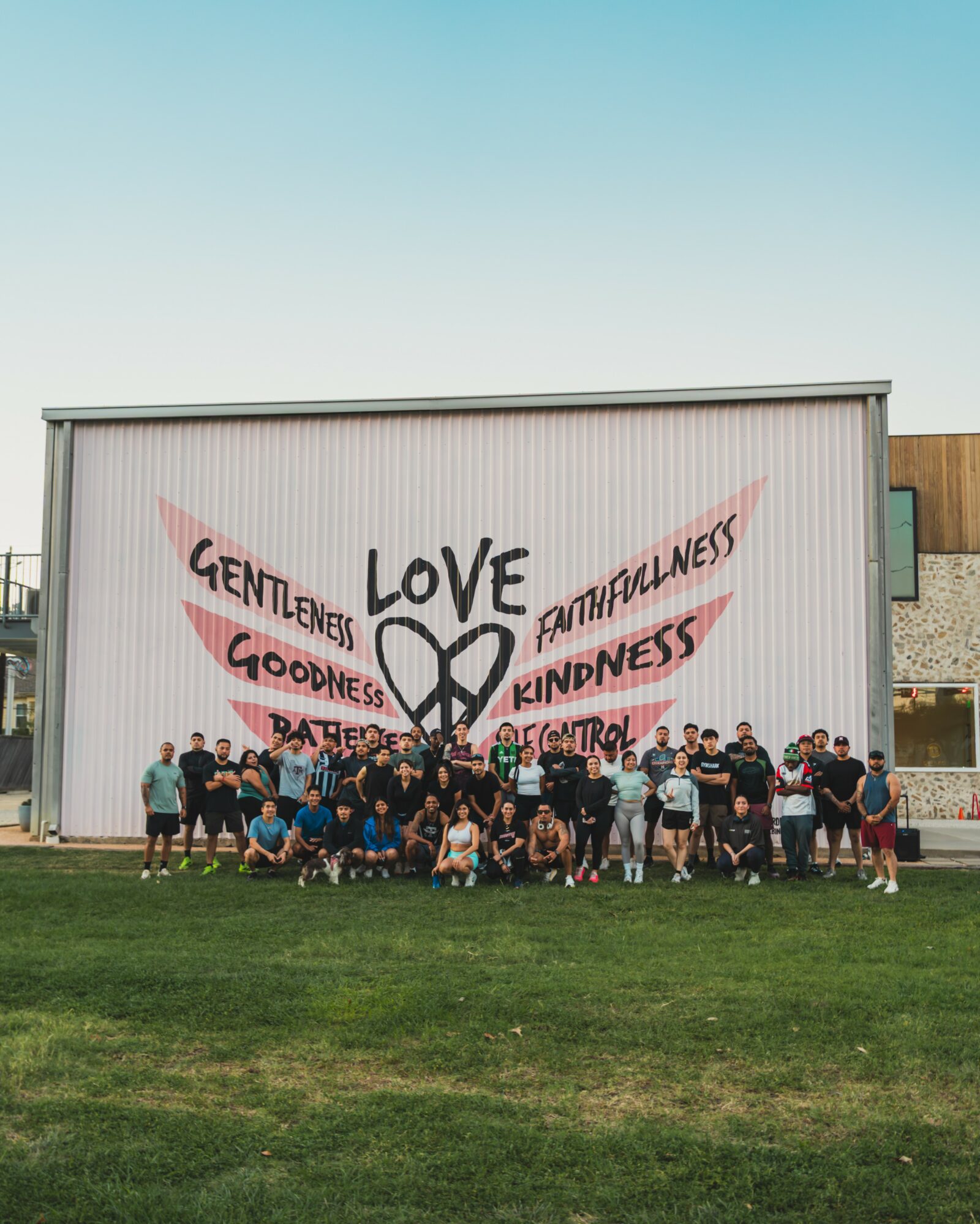 Group of people standing in front of a wall with a large heart and words like love, kindness, goodness, faithfulness, patience, and self-control.