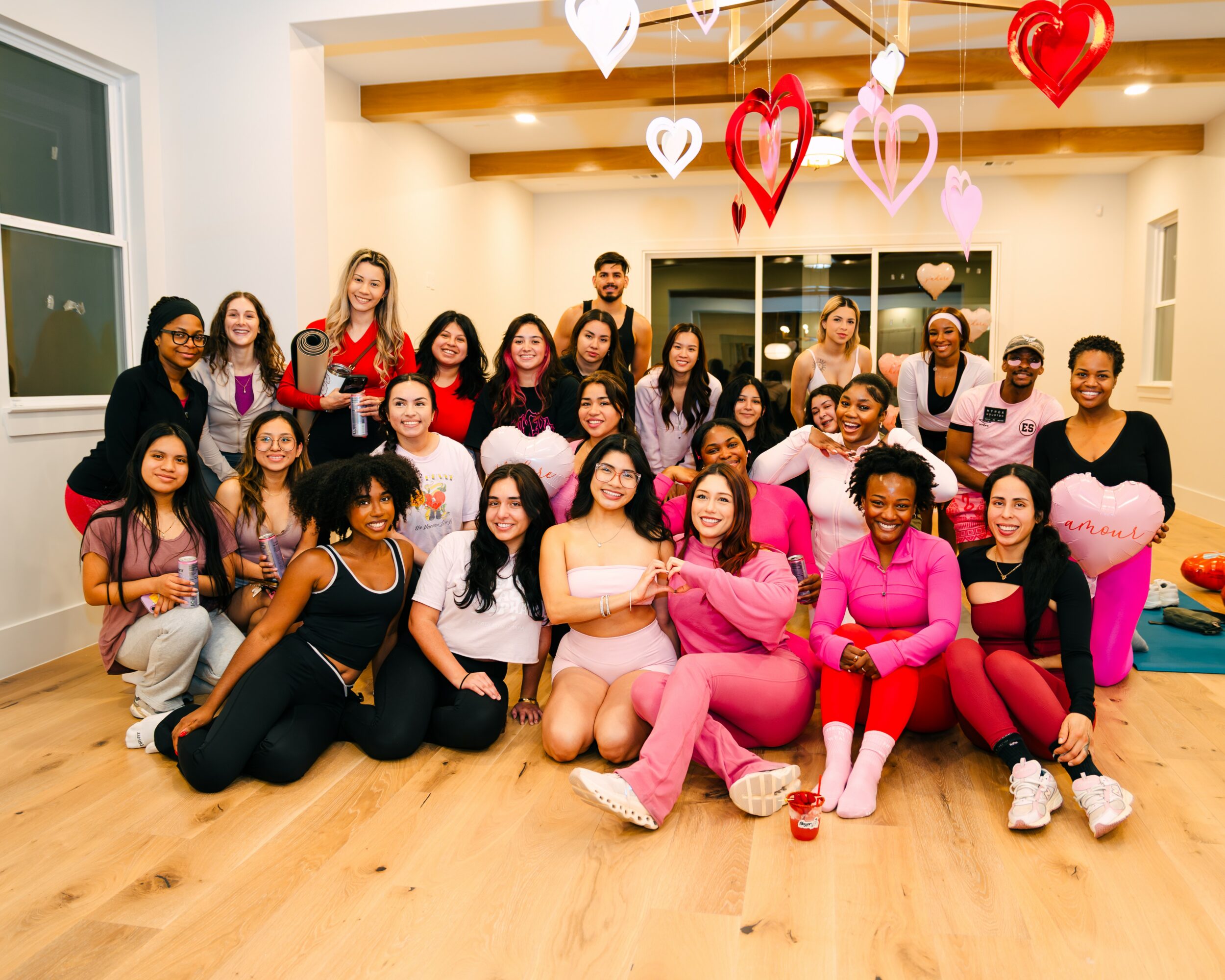 Group of women and men celebrating with heart-shaped decorations hanging from ceiling, smiling in a brightly lit room.