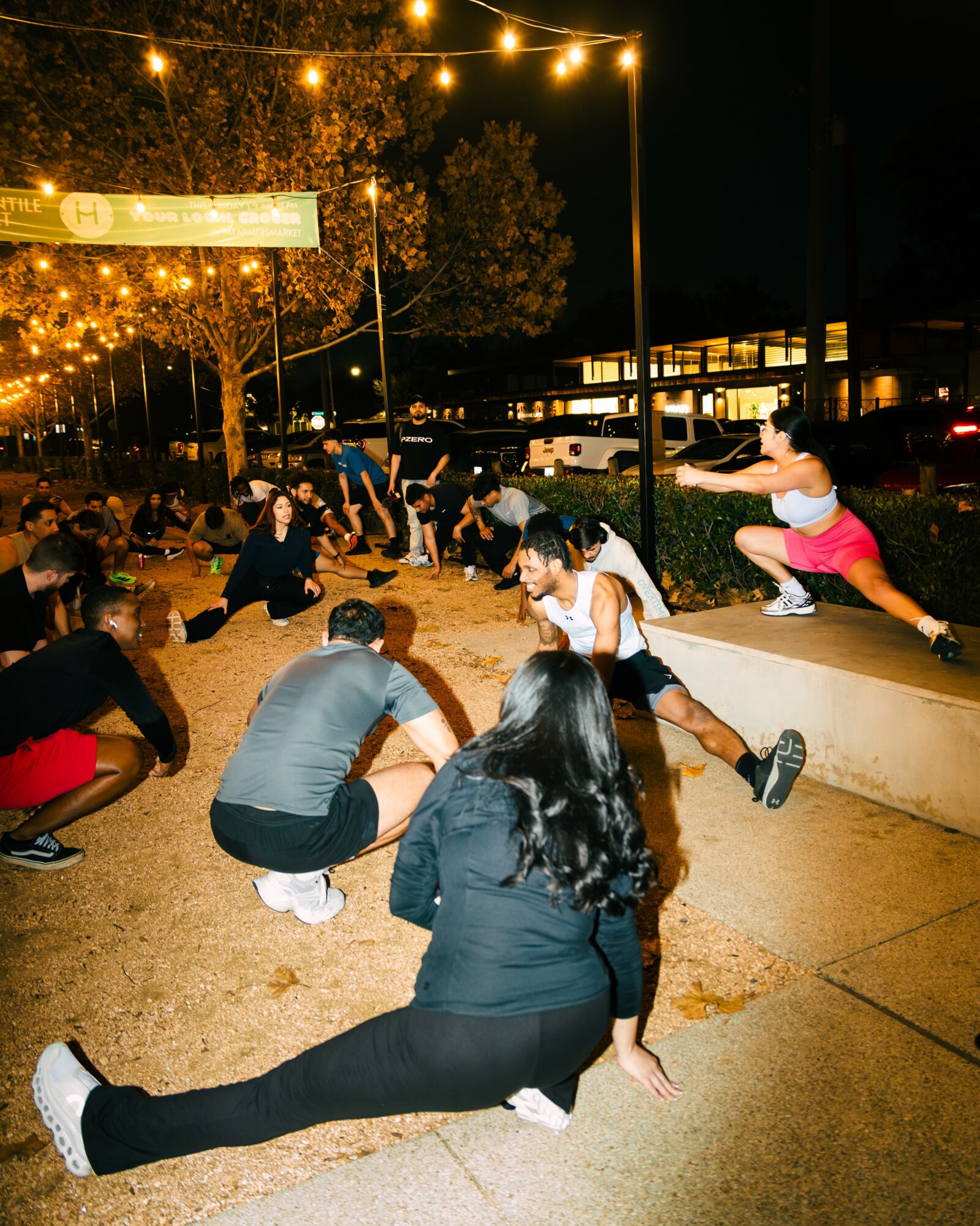 People participating in an outdoor activity at night, with string lights overhead and a building in the background.