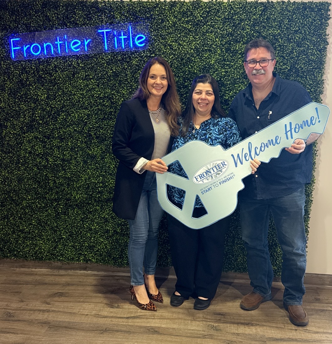 Three people standing in front of a green wall, holding a large key-shaped sign that says 