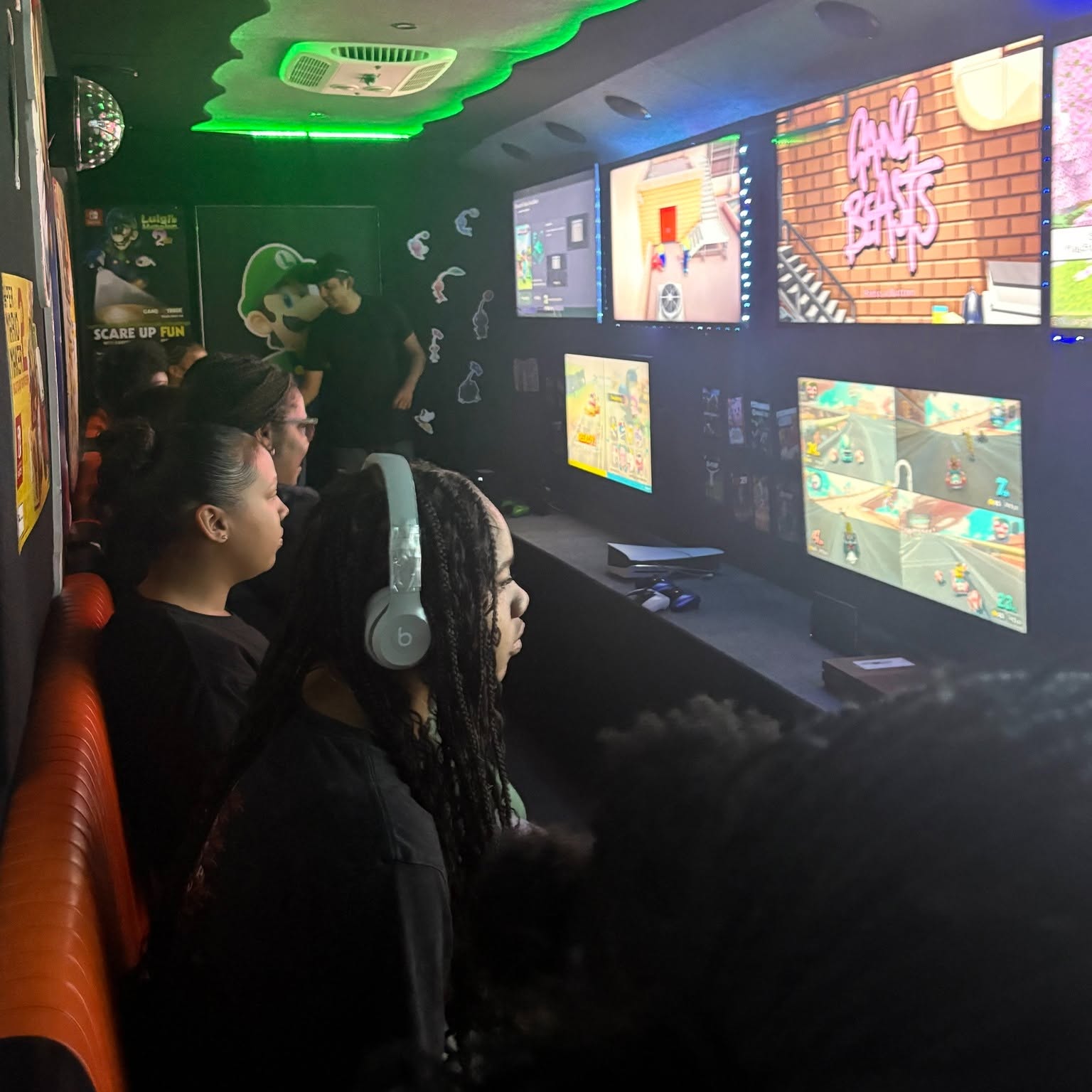 Group of people playing video games in a gaming arcade with multiple screens and neon lighting.