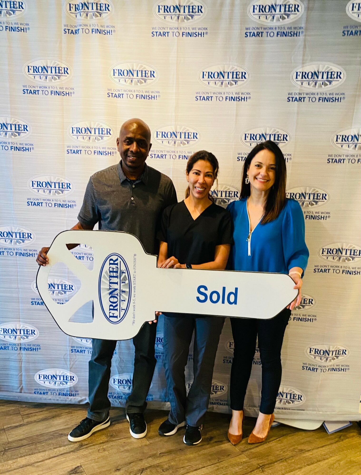 Three people holding a large key-shaped sign that says 'Sold' in front of a backdrop with 'Frontier' logos.