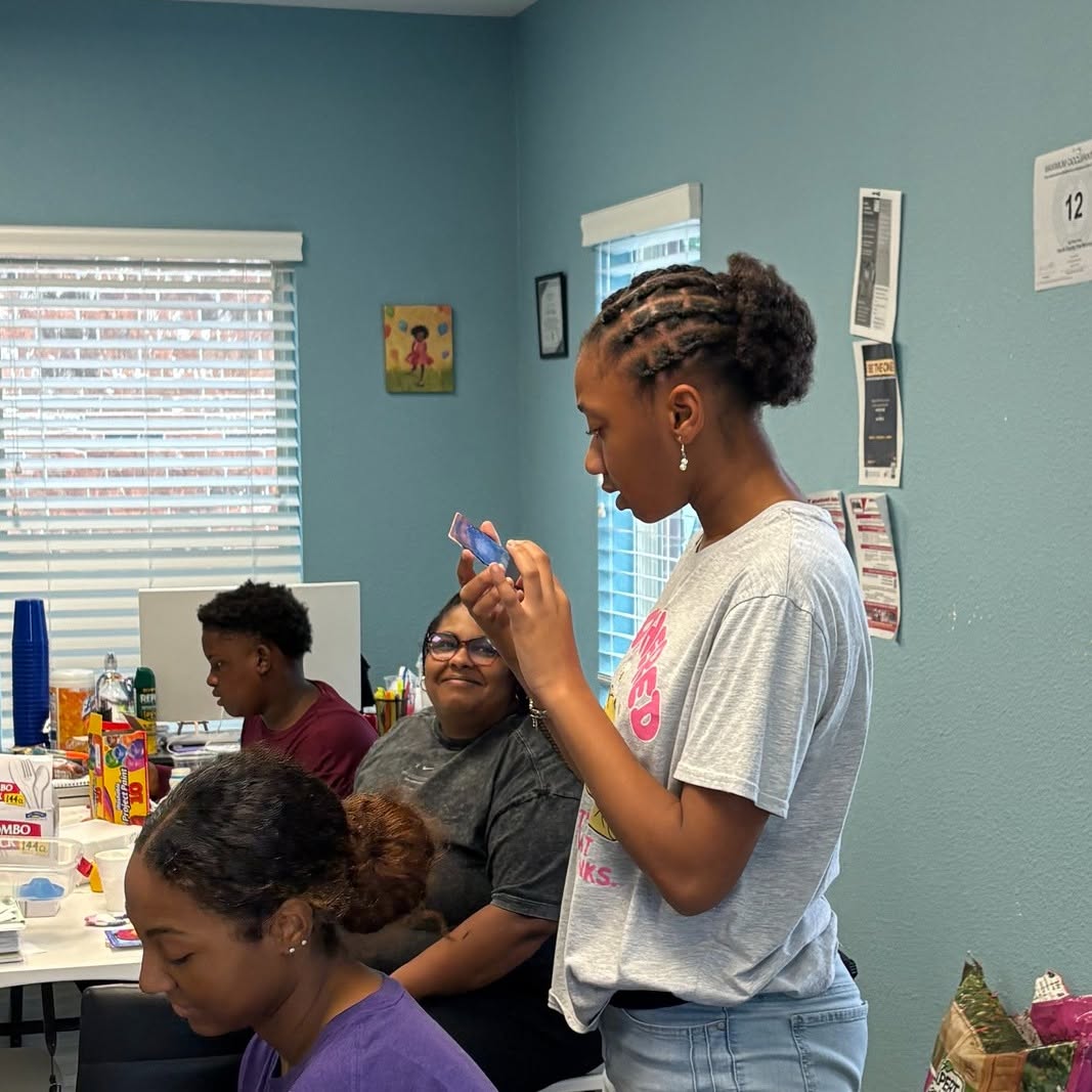 Four people in a room with blue walls, two women and two children, engaging with each other and objects on a table.