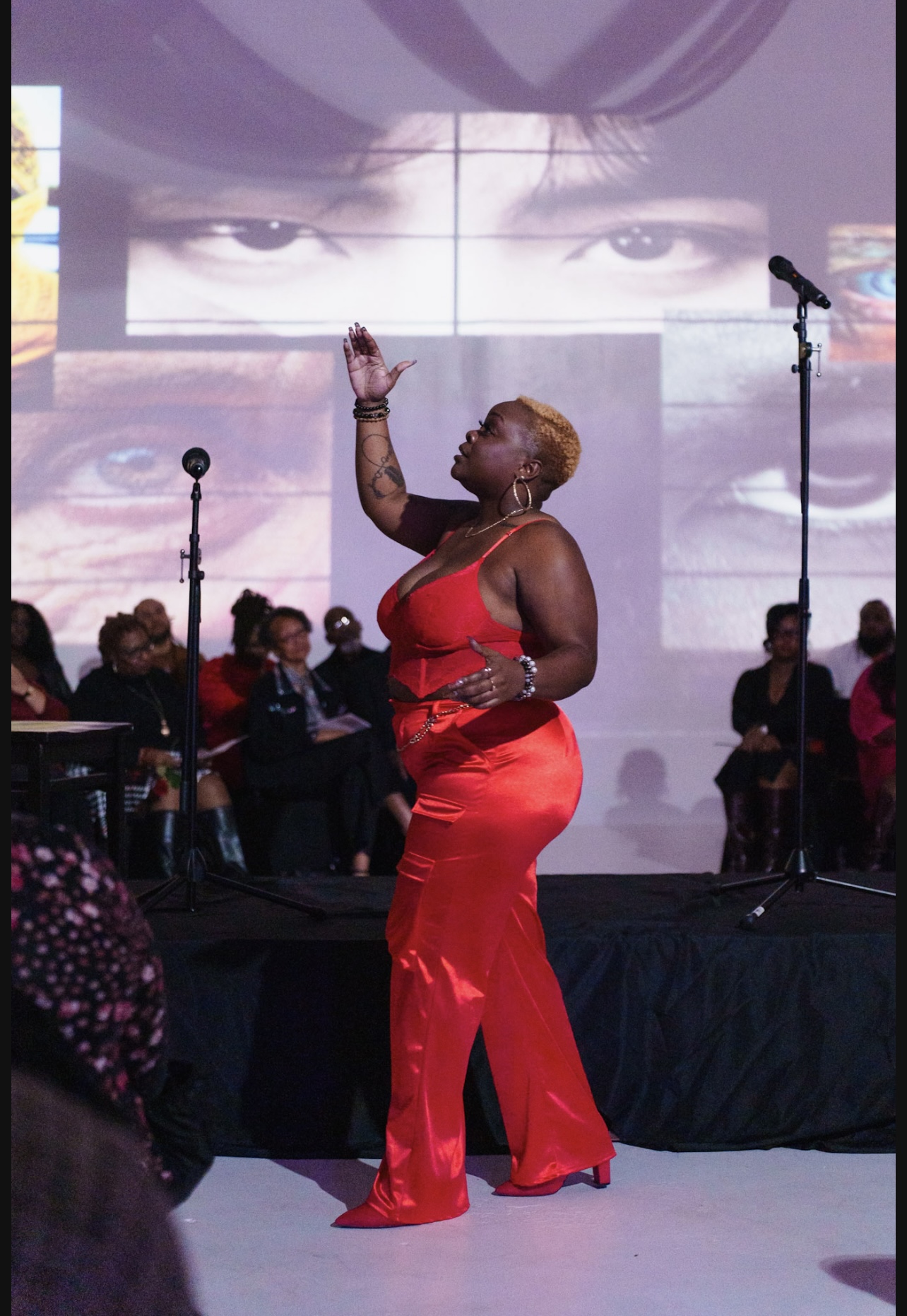 A woman in a red dress performs on stage with a band, large screens showing eyes behind her.