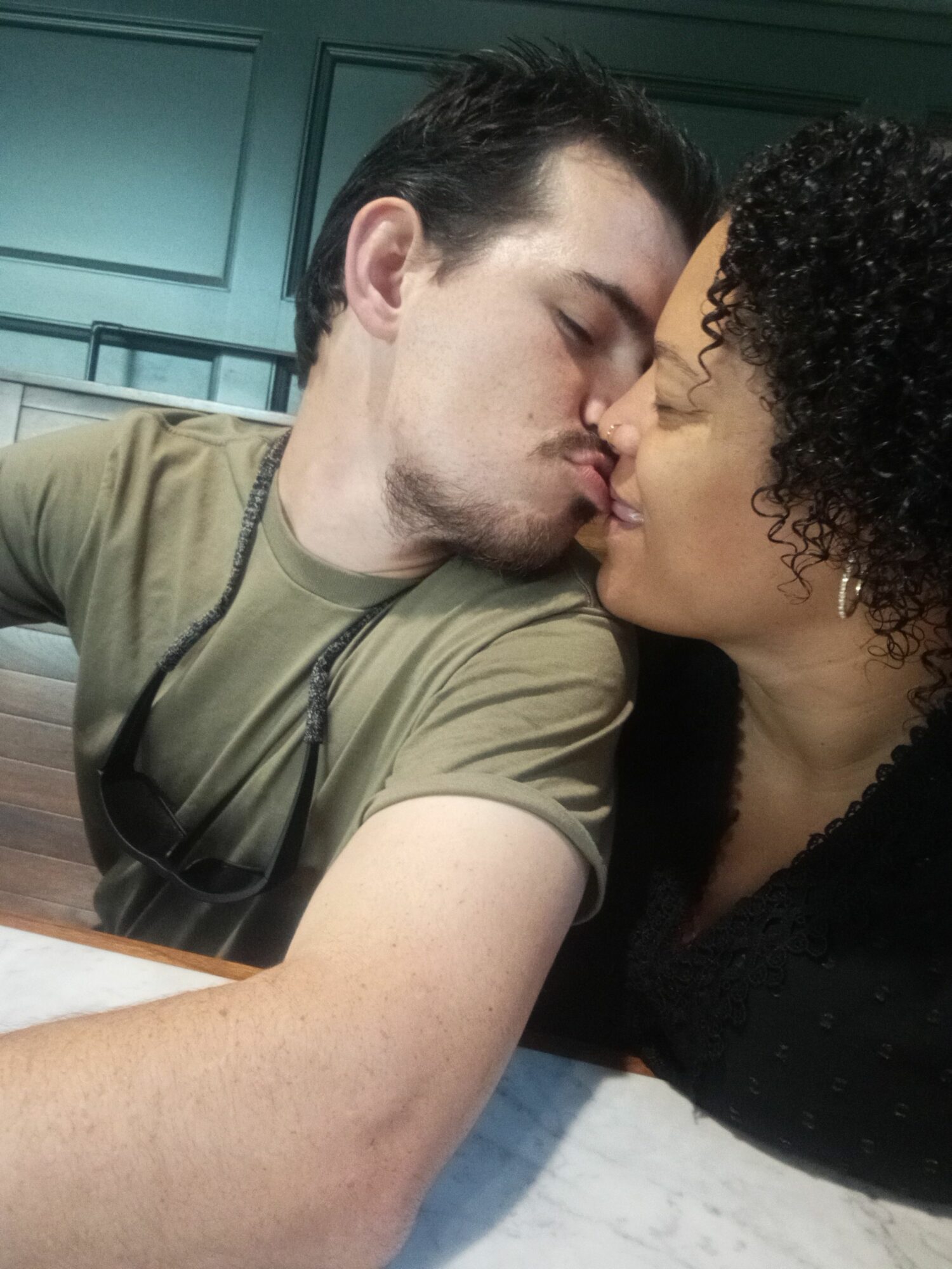 Two people are lying down close, about to kiss, with a background of green cabinets and a blue wall.
