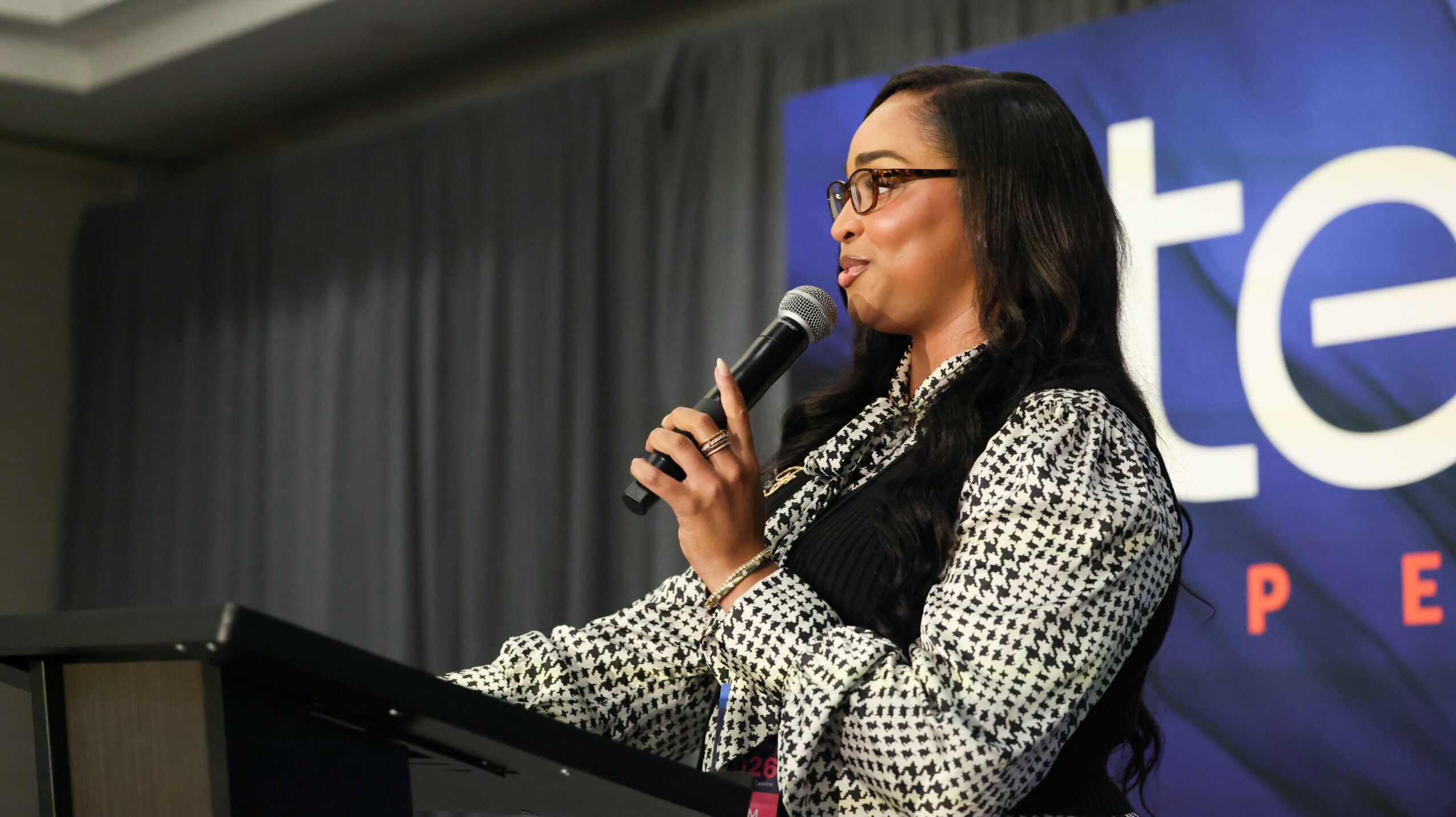Woman speaking into a microphone at a podium during a presentation or event.