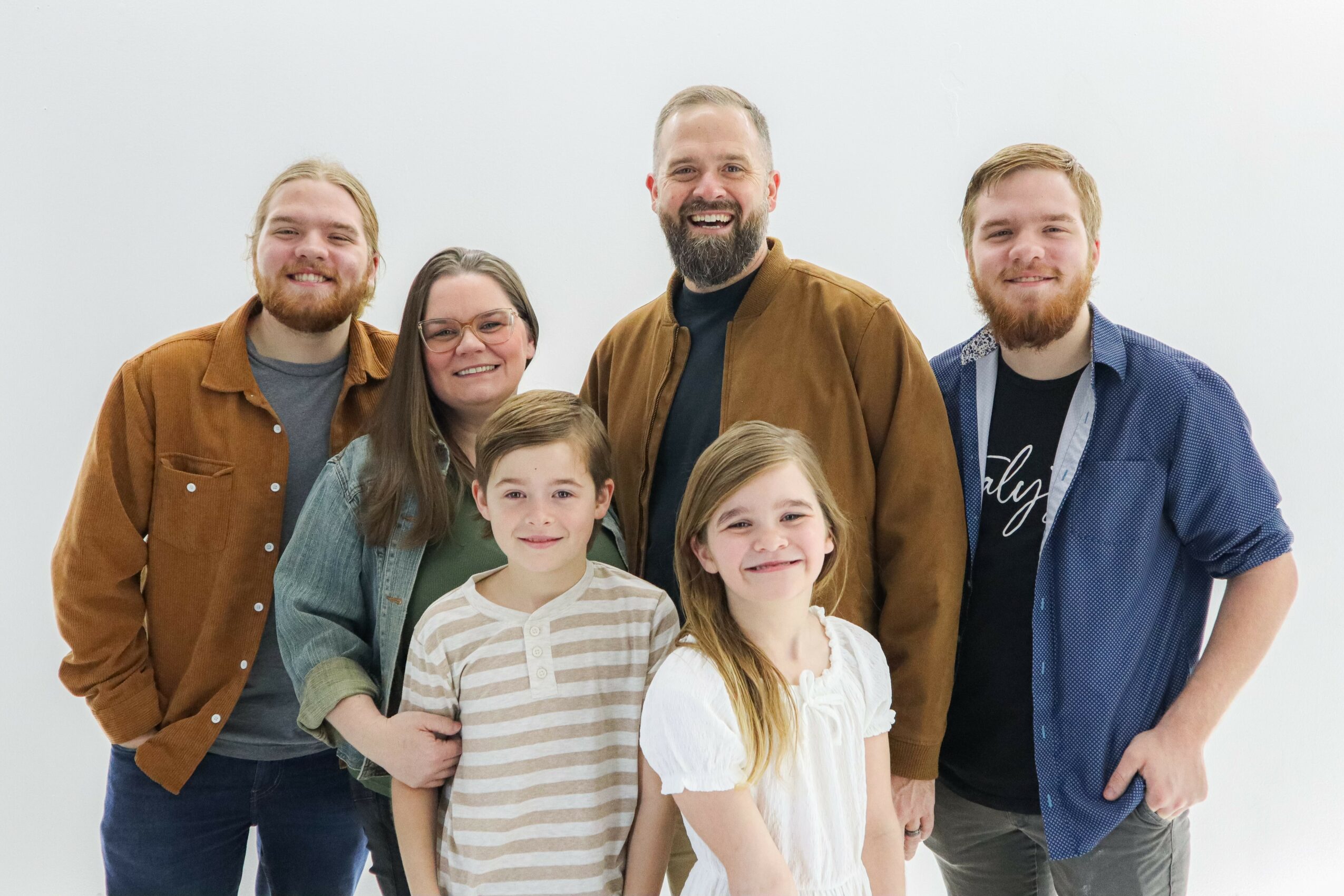 Group of six people smiling, standing together against a plain background.
