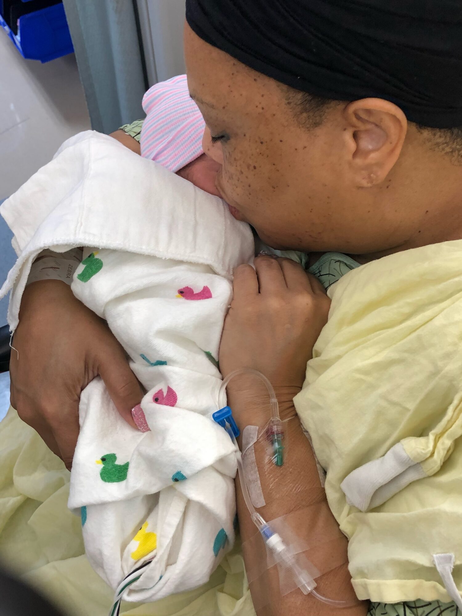 Adult holding a newborn baby in a hospital, both resting, with medical tubes attached to the baby.