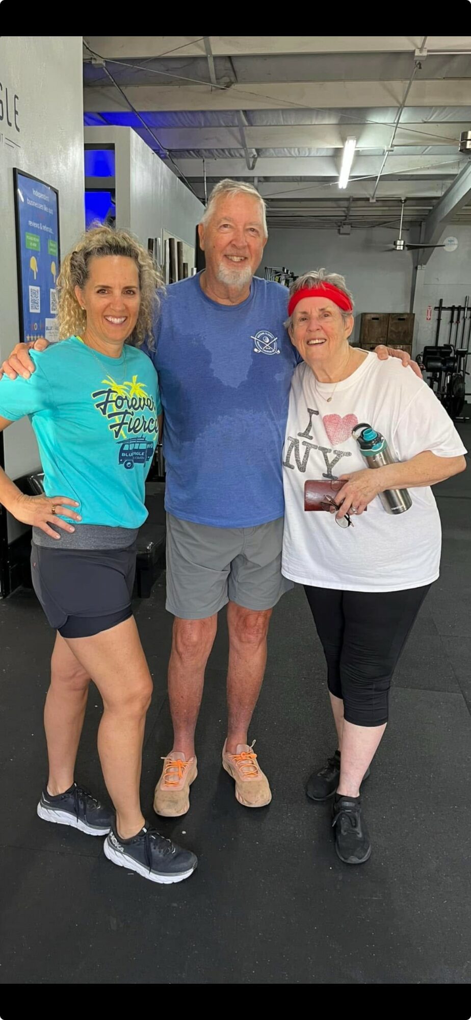 Three people standing together in a gym, smiling, with gym equipment in background.