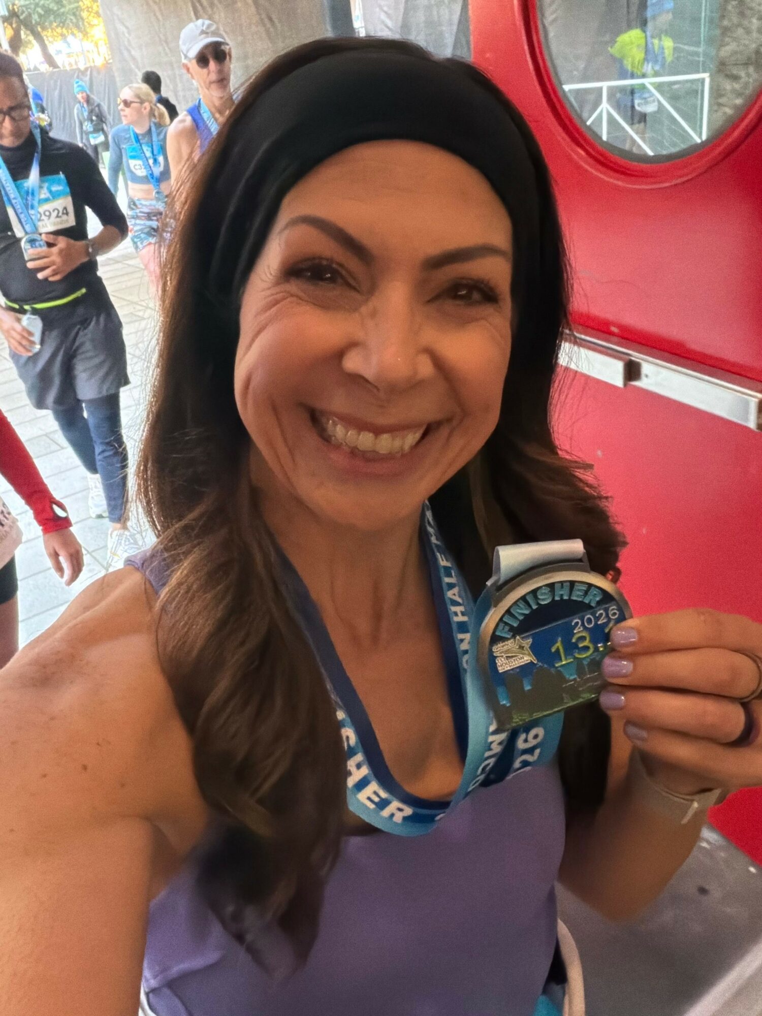 Woman smiling, holding a medal, with people and a red structure in the background.