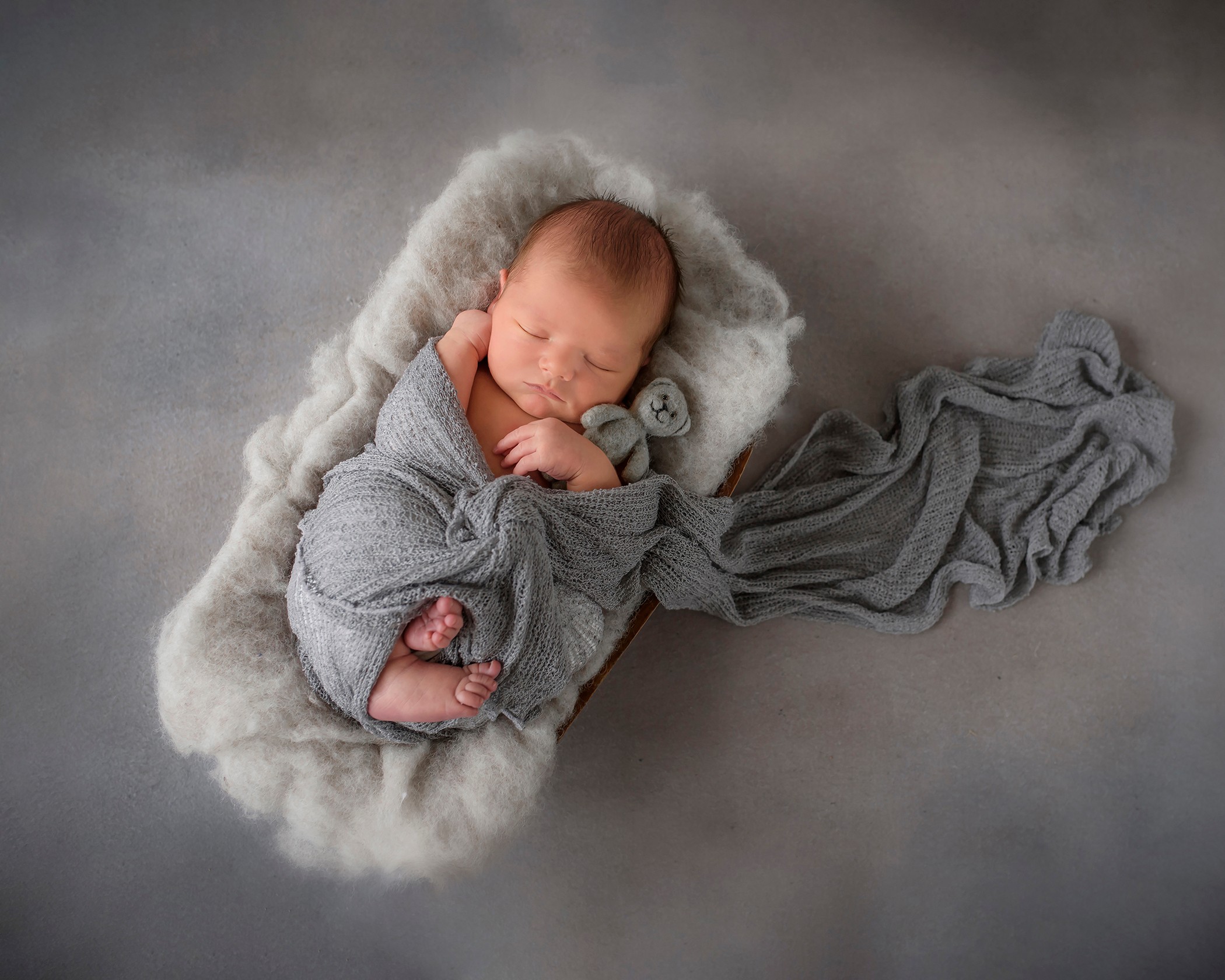 Newborn baby sleeping on soft blanket, wrapped in gray cloth, with a gray fabric extending to the right.