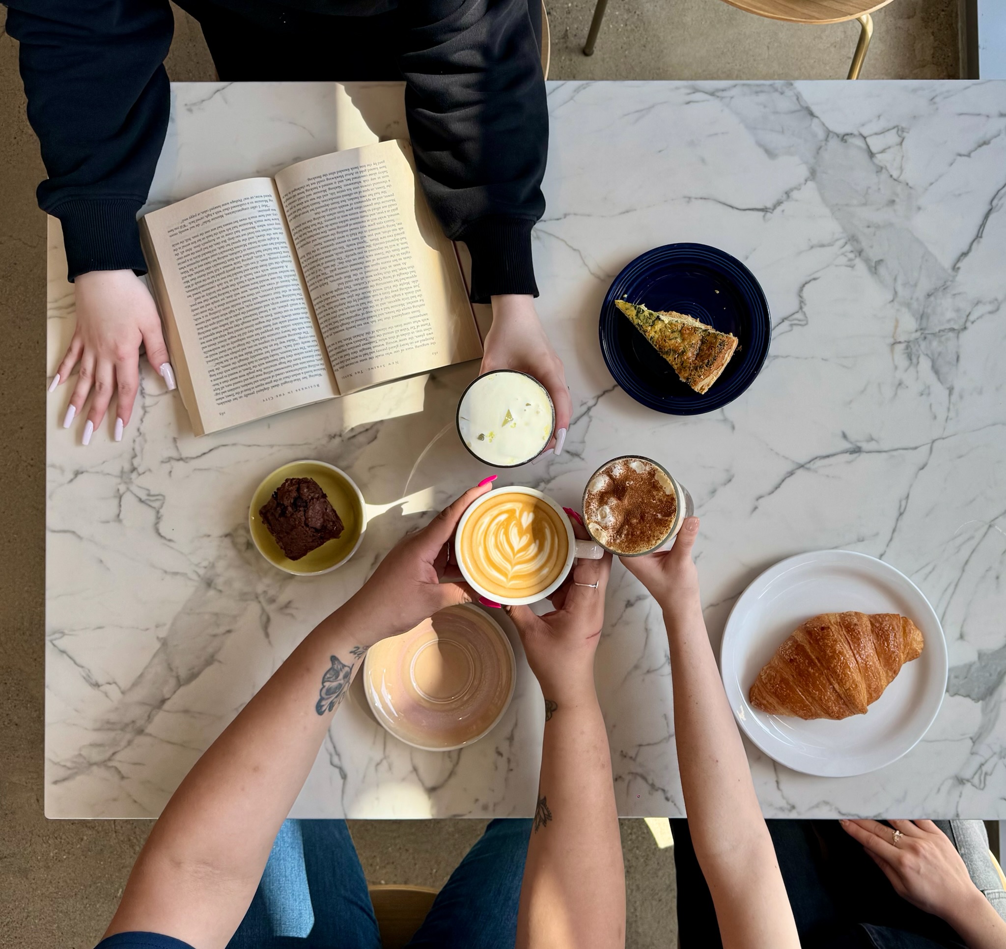 People at a marble table with books, drinks, and a croissant, seen from above.