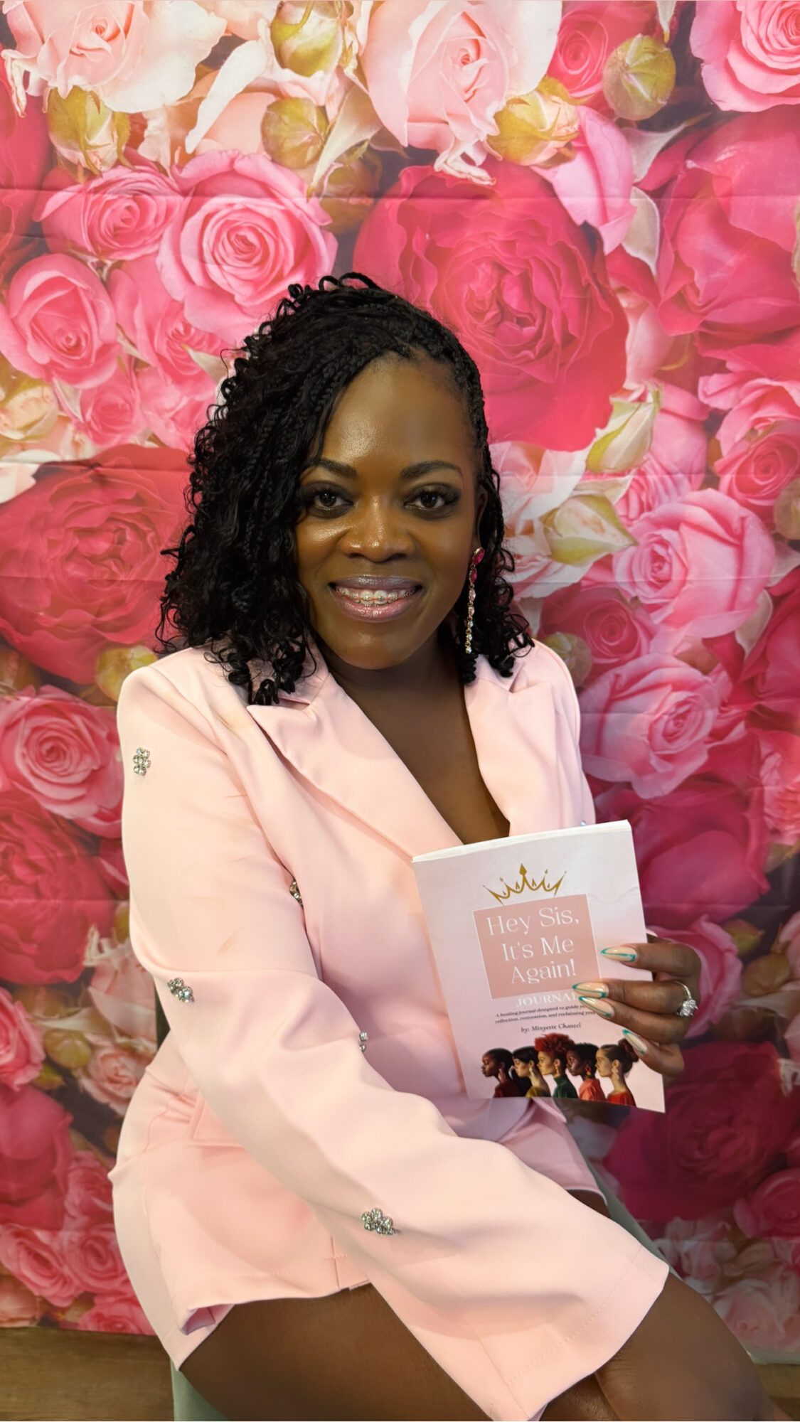 Woman with curly hair holding a card, standing in front of a pink floral background.