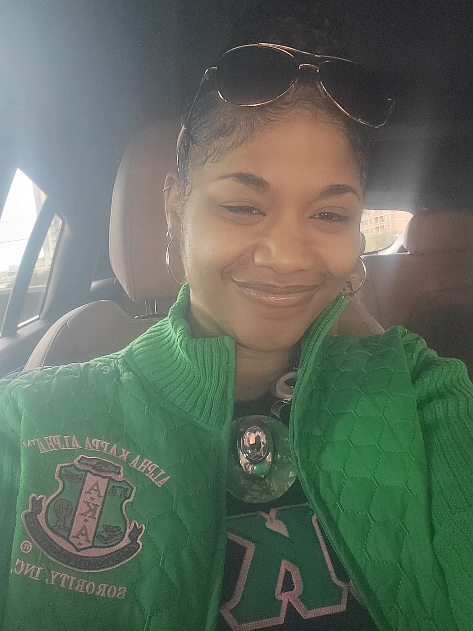Smiling woman wearing sunglasses on head and green jacket inside a car.