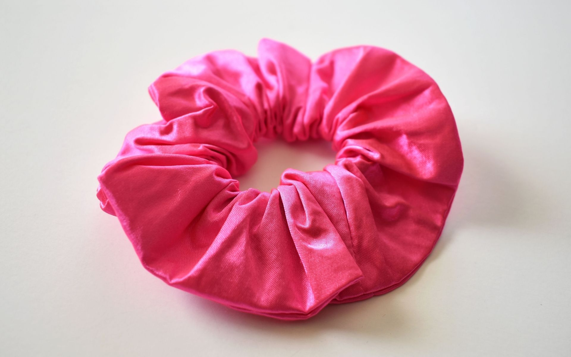 Pink fabric scrunchie on a white surface, gathered elastic band for hair styling.