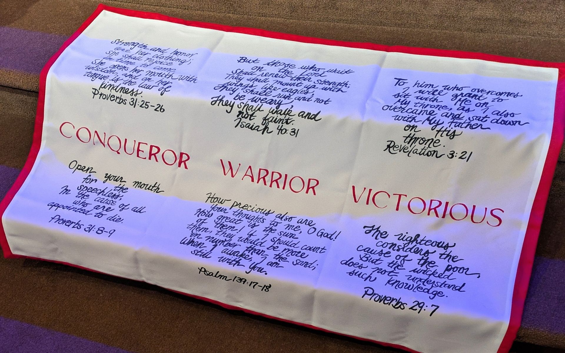 A paper with handwritten notes and printed words, including 'CONQUEROR,' 'WARRIOR,' and 'VICTORIOUS,' on a red-bordered surface.
