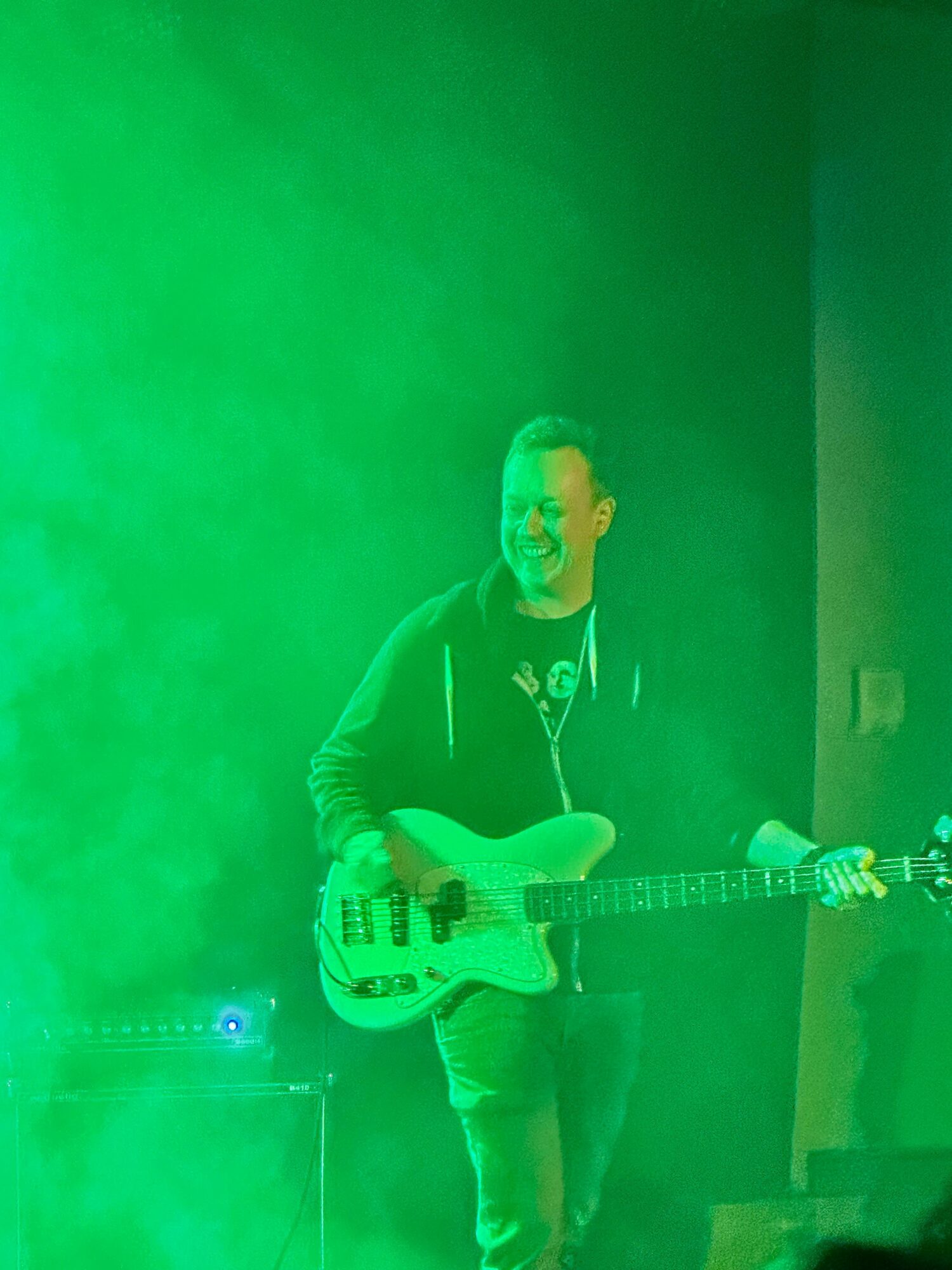 Person holding an electric guitar, standing in a room with green lighting, facing forward.