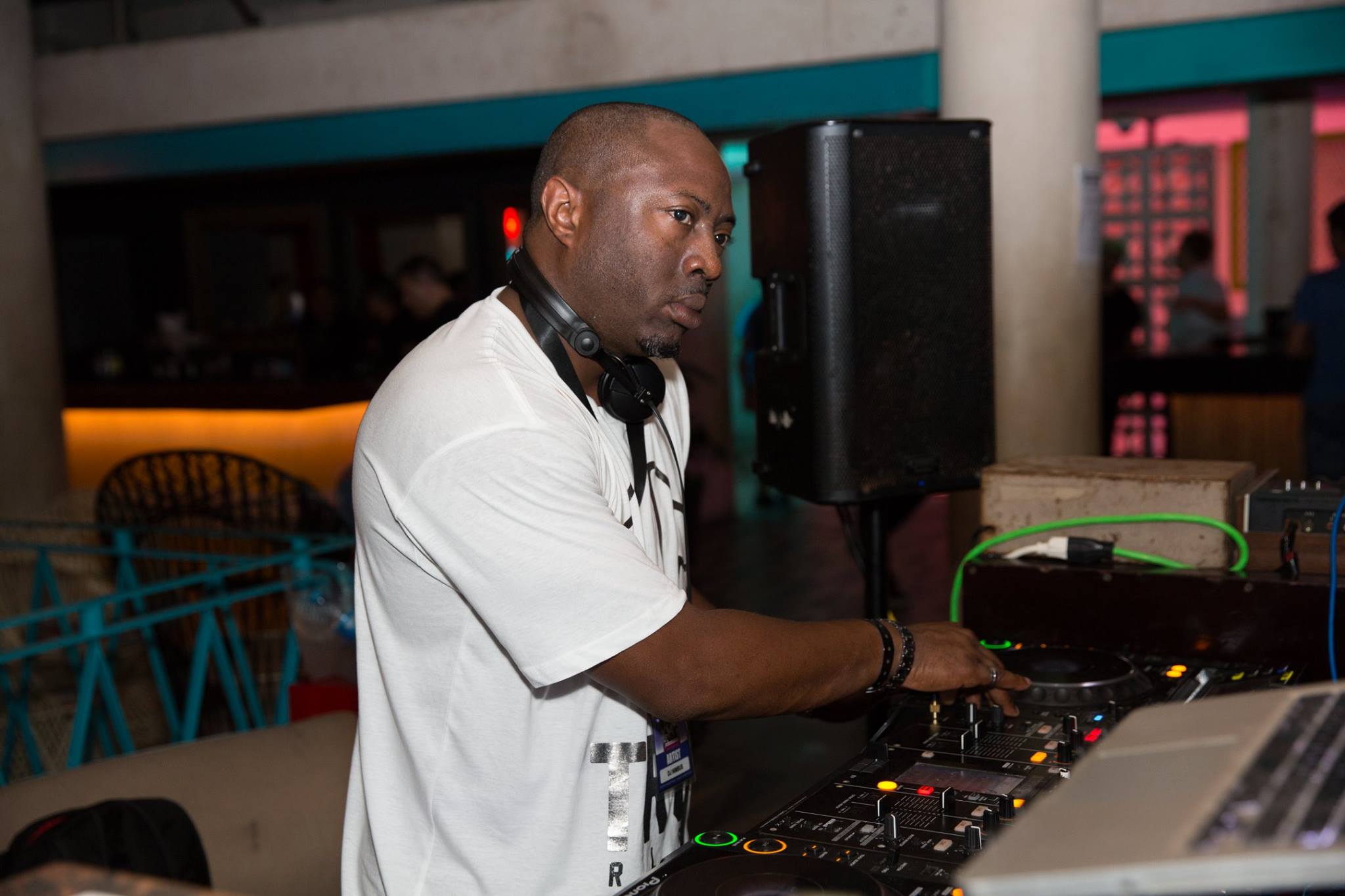 DJ wearing a white shirt and headphones, operating DJ equipment in a dimly lit indoor venue.