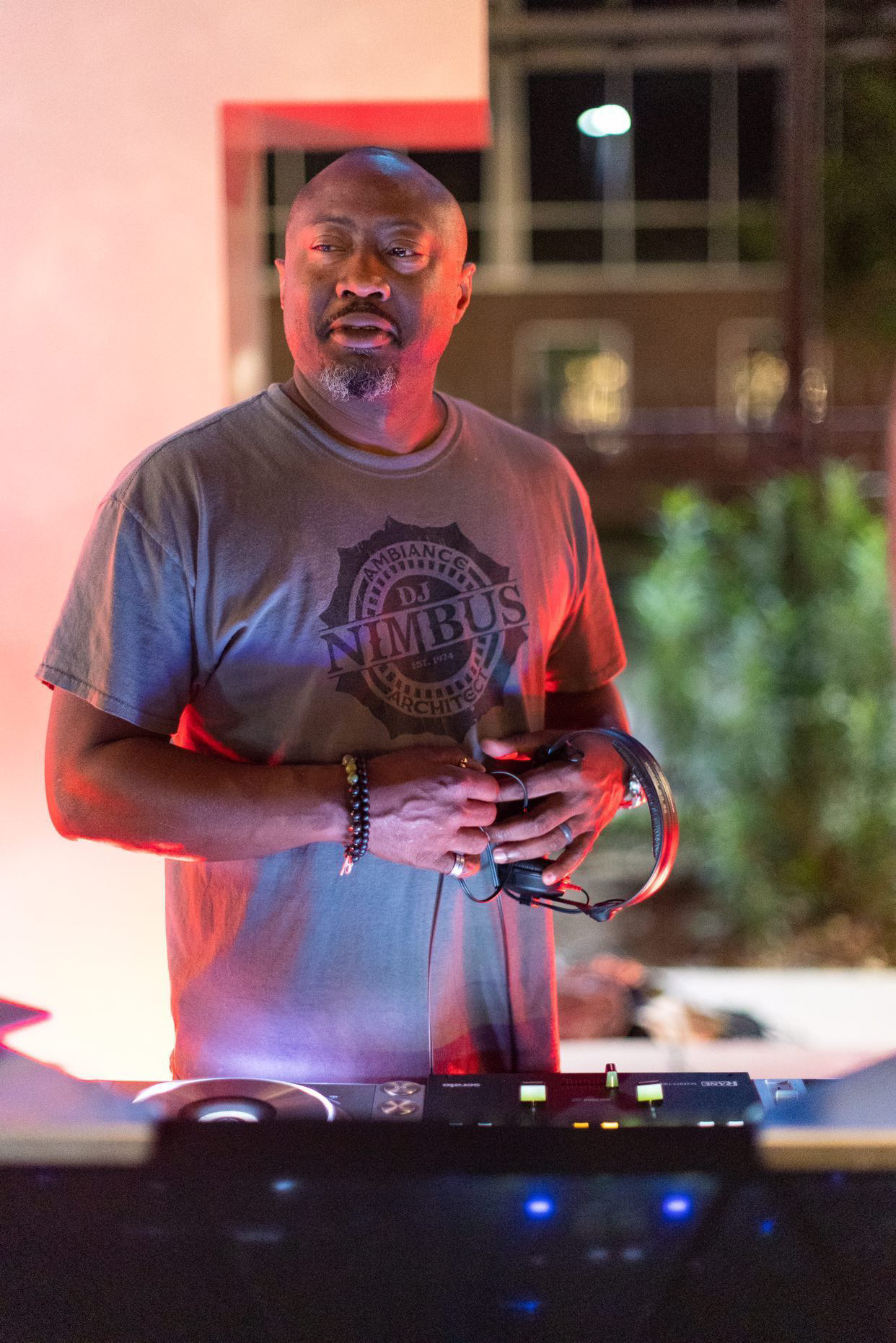 Man with short hair and beard wearing a gray T-shirt with a logo, standing outdoors at night, holding a phone.