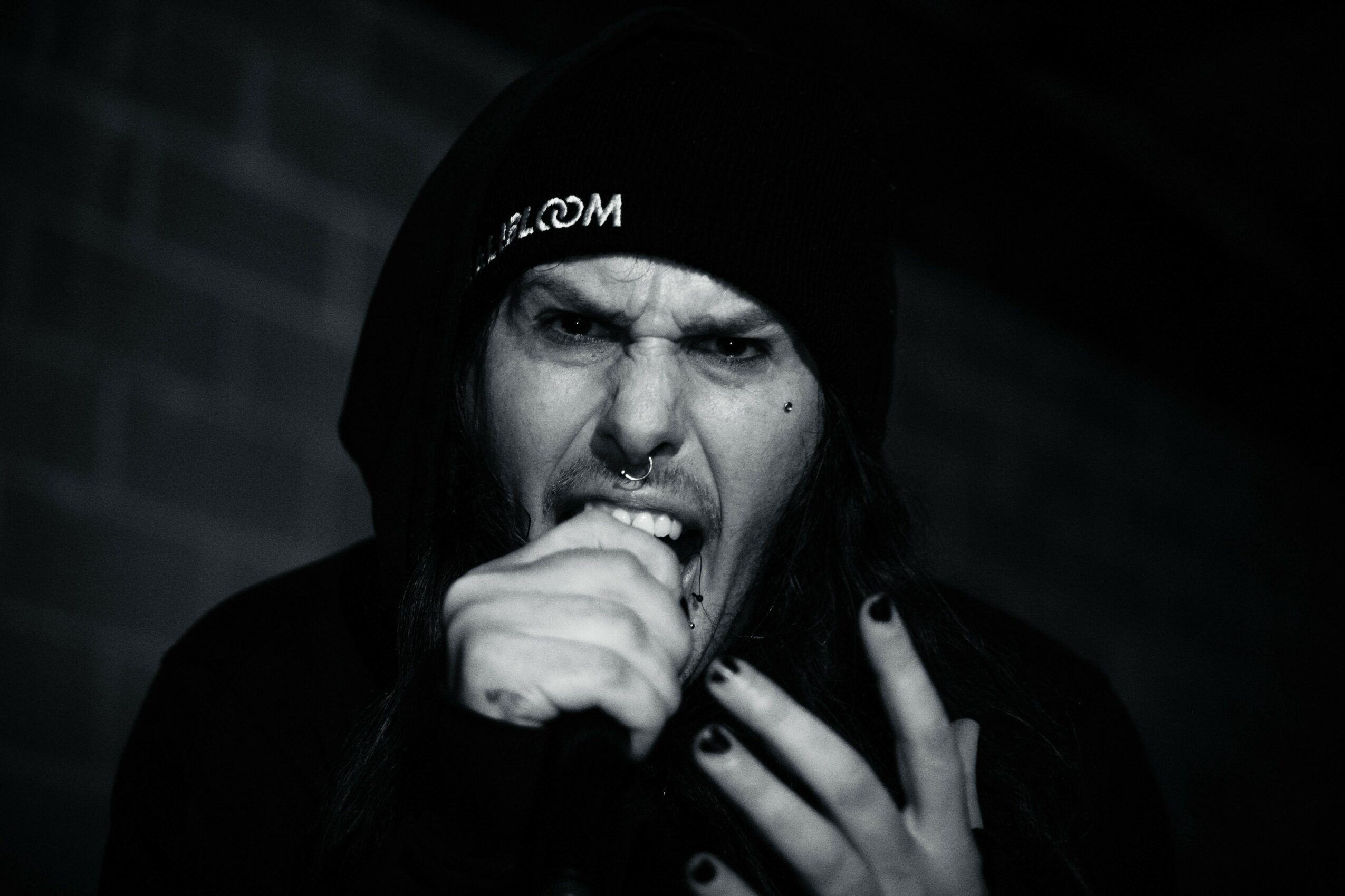 Person with long hair wearing a beanie, biting their finger, with a dark background.