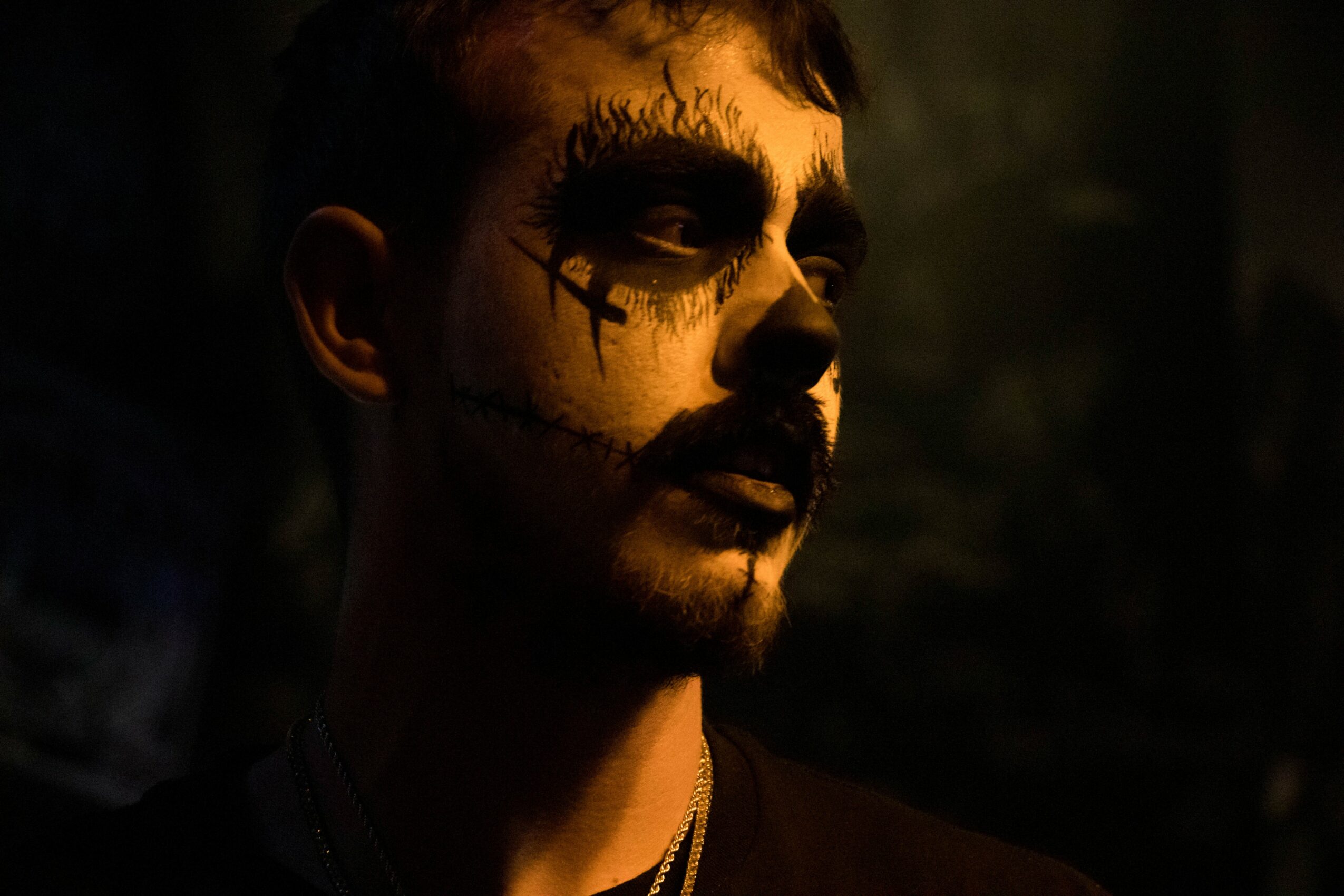Person with face painted in a skull design, dark background, looking to the side, dramatic lighting.