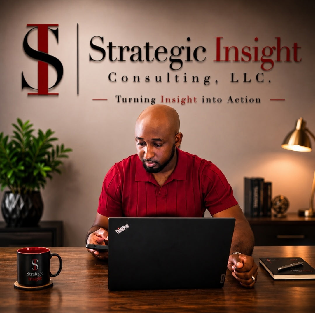 Man in red shirt working on laptop at desk with company logo and plants in background.