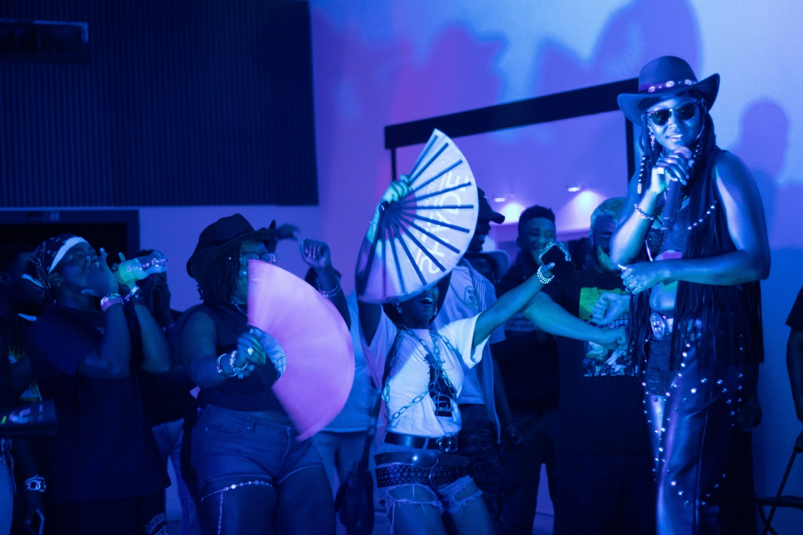 Group of people in costumes, some with umbrellas, in a dark, colorful setting, possibly a performance or party.