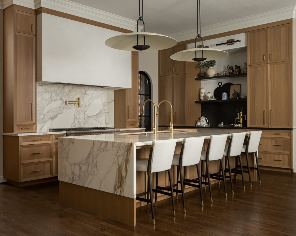 Kitchen with marble island, wooden cabinets, black open shelves, and four white chairs at the island, pendant lights above.