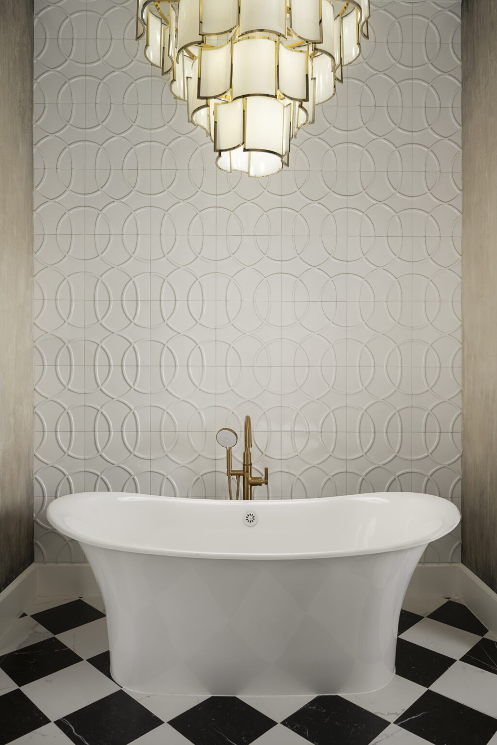 Elegant bathroom with a freestanding bathtub, gold faucet, patterned wall, and a large chandelier overhead.