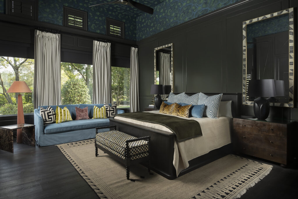 Bedroom with large windows, a bed with pillows, a blue sofa, and two mirrors on the wall.