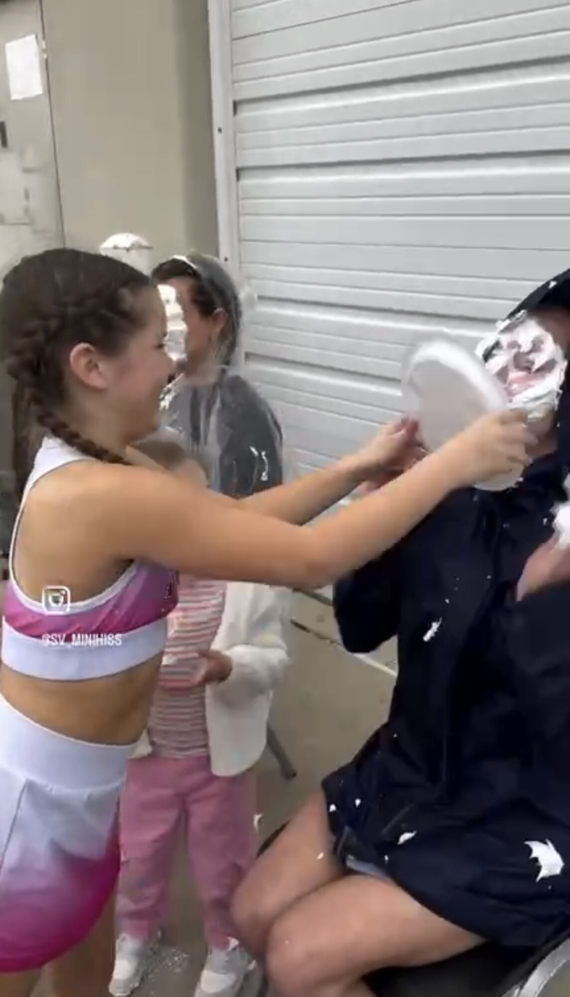 Girl splashes water on a person sitting, with two children watching in background, in an indoor setting.