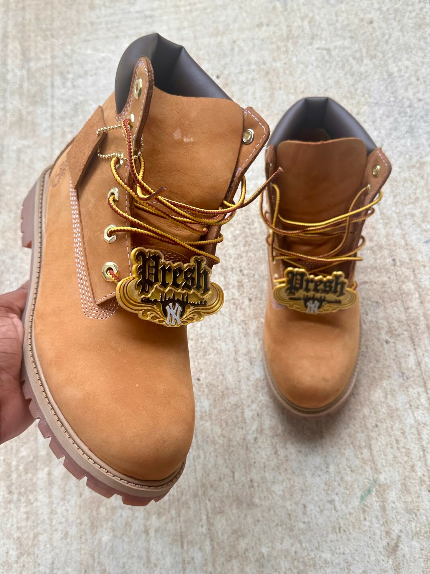 Pair of tan work boots with gold chains and tags, placed on a light-colored surface.