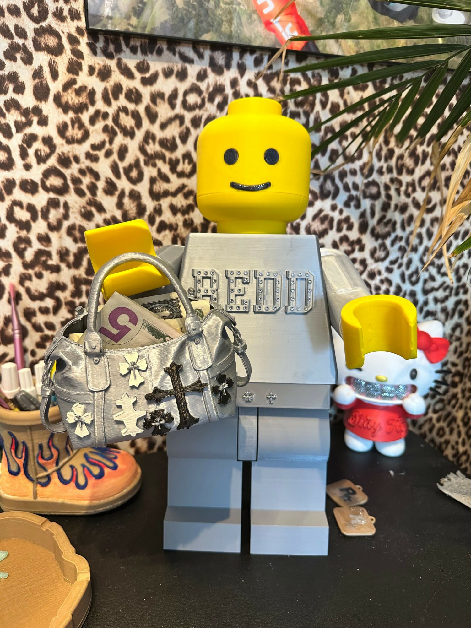 Collection of toys including a yellow block character, a Hello Kitty figure, a metallic robot, and a shoe, on a leopard print surface.