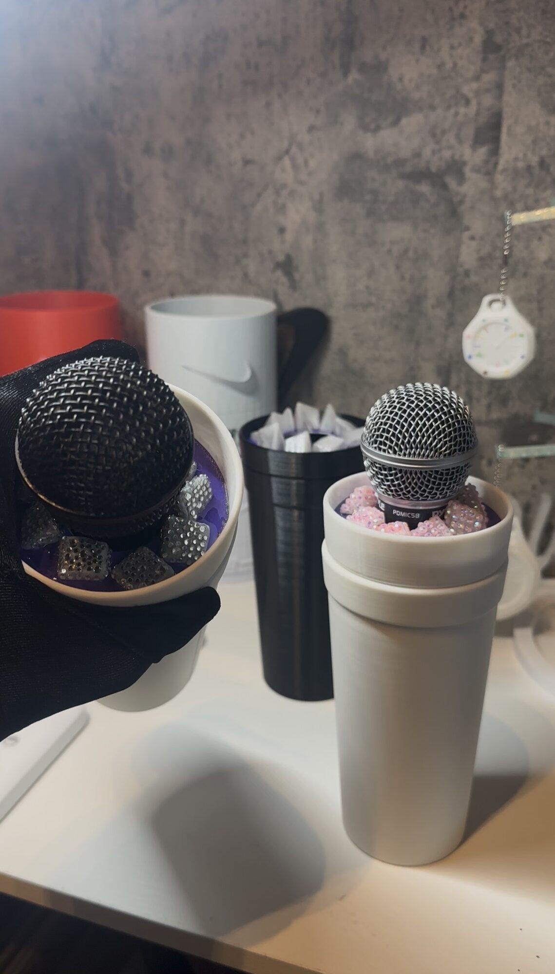 Two microphones in cups on a white surface, with a gray textured wall in the background.