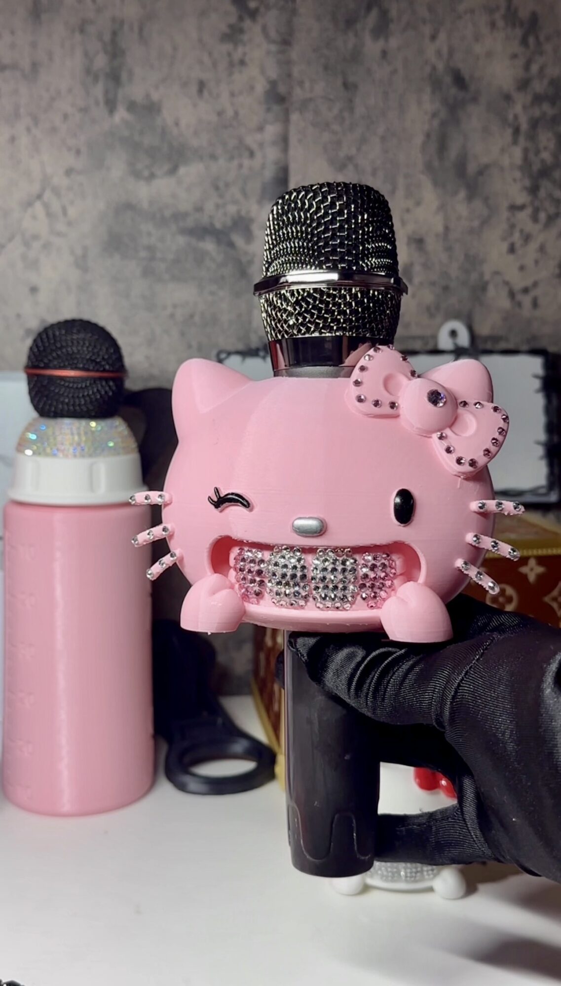 Pink pig-shaped speaker with a smiling face, surrounded by microphones and a black object, against a textured wall.