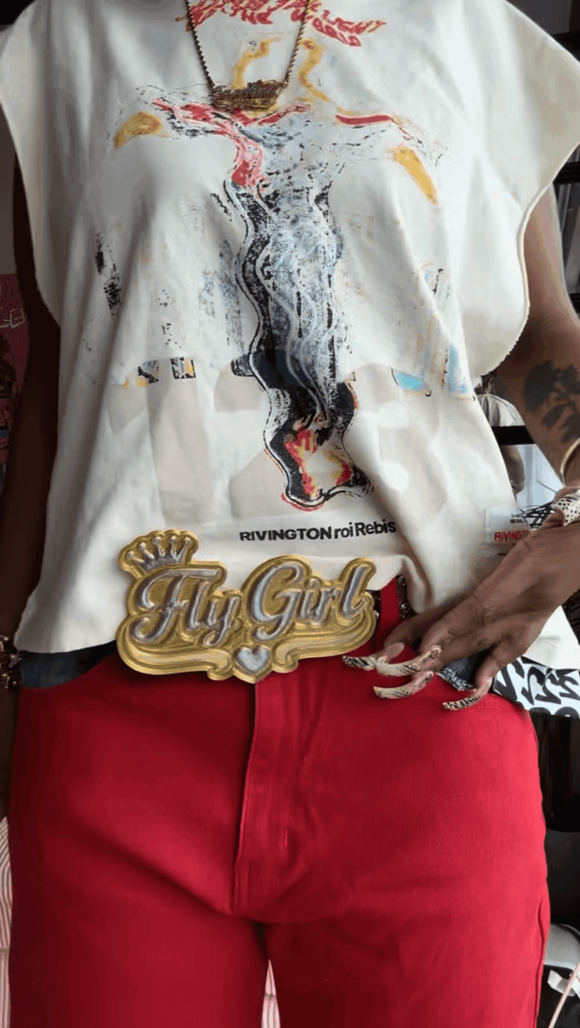 Person wearing a graphic T-shirt with a colorful design, red pants, and a gold belt buckle that says 'Yay Girl'.