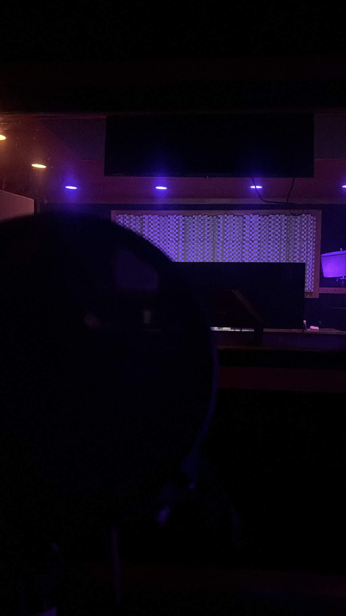 Stage with purple and blue lighting, large screen, and patterned backdrop, in a dark venue.