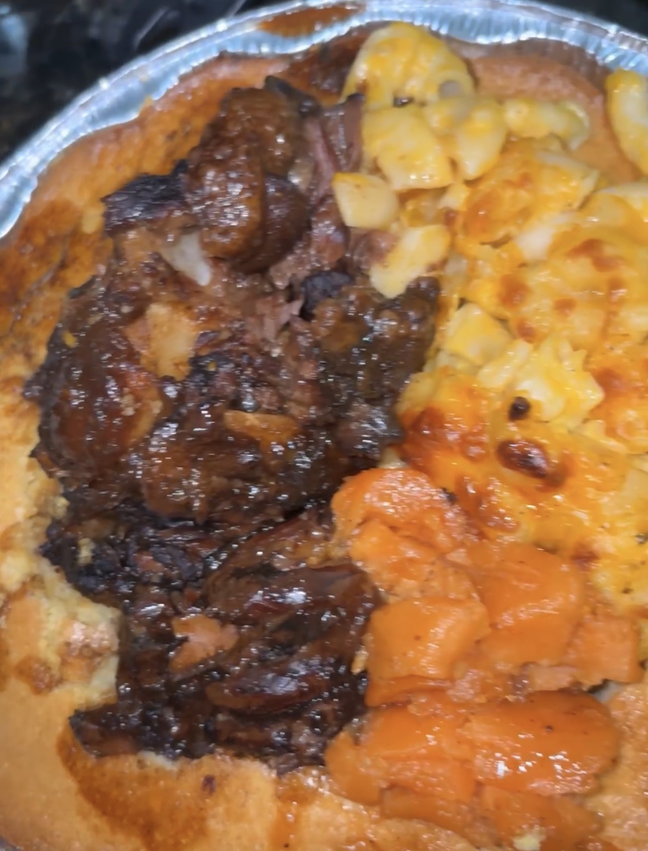 Close-up of a pizza with dark meat, pasta, and cheese toppings, in a foil container.