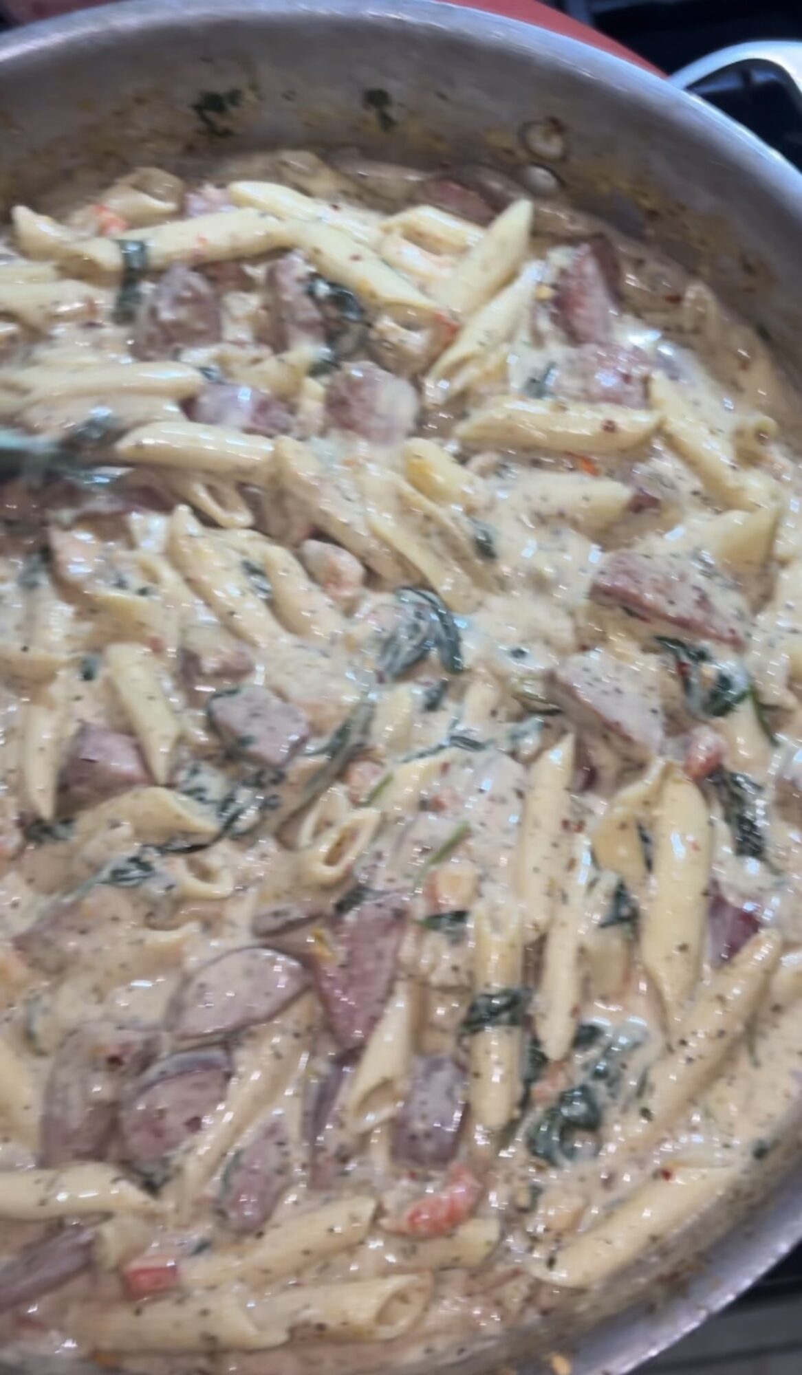 Creamy pasta with pieces of meat and vegetables in a pan.