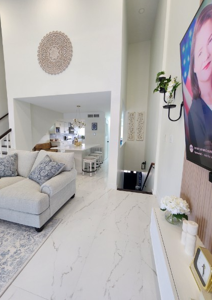 Living room with white sofa, decorative pillows, wall art, and a view into the kitchen area, with a white marble floor.