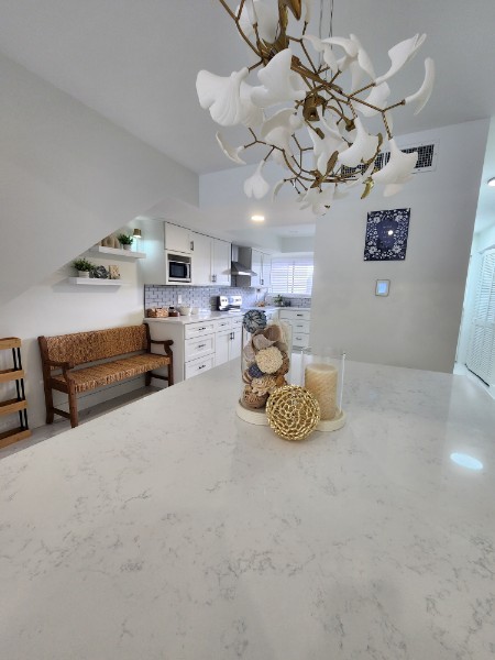 Kitchen and dining area with white walls, a wooden bench, and decorative items on a white table.
