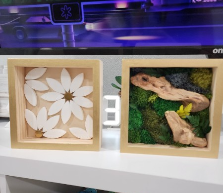 Two decorative boxes with natural elements, one with white leaves and the other with rocks and moss, on a white surface.