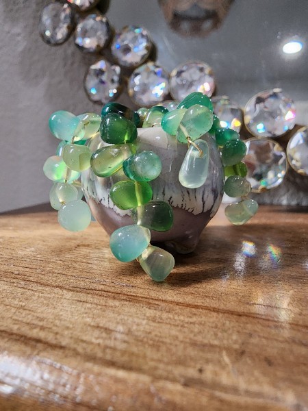 Small decorative glass beads in green, blue, and clear colors arranged on a wooden surface with a reflective background.