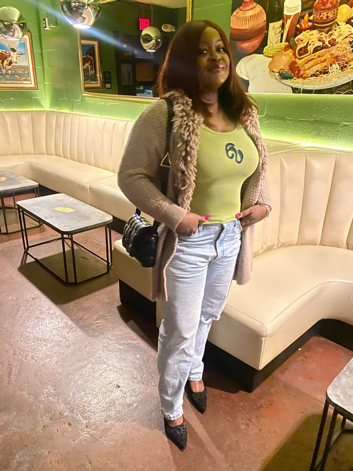 Woman standing in a room with a beige sofa, green counter, and framed pictures on the wall.