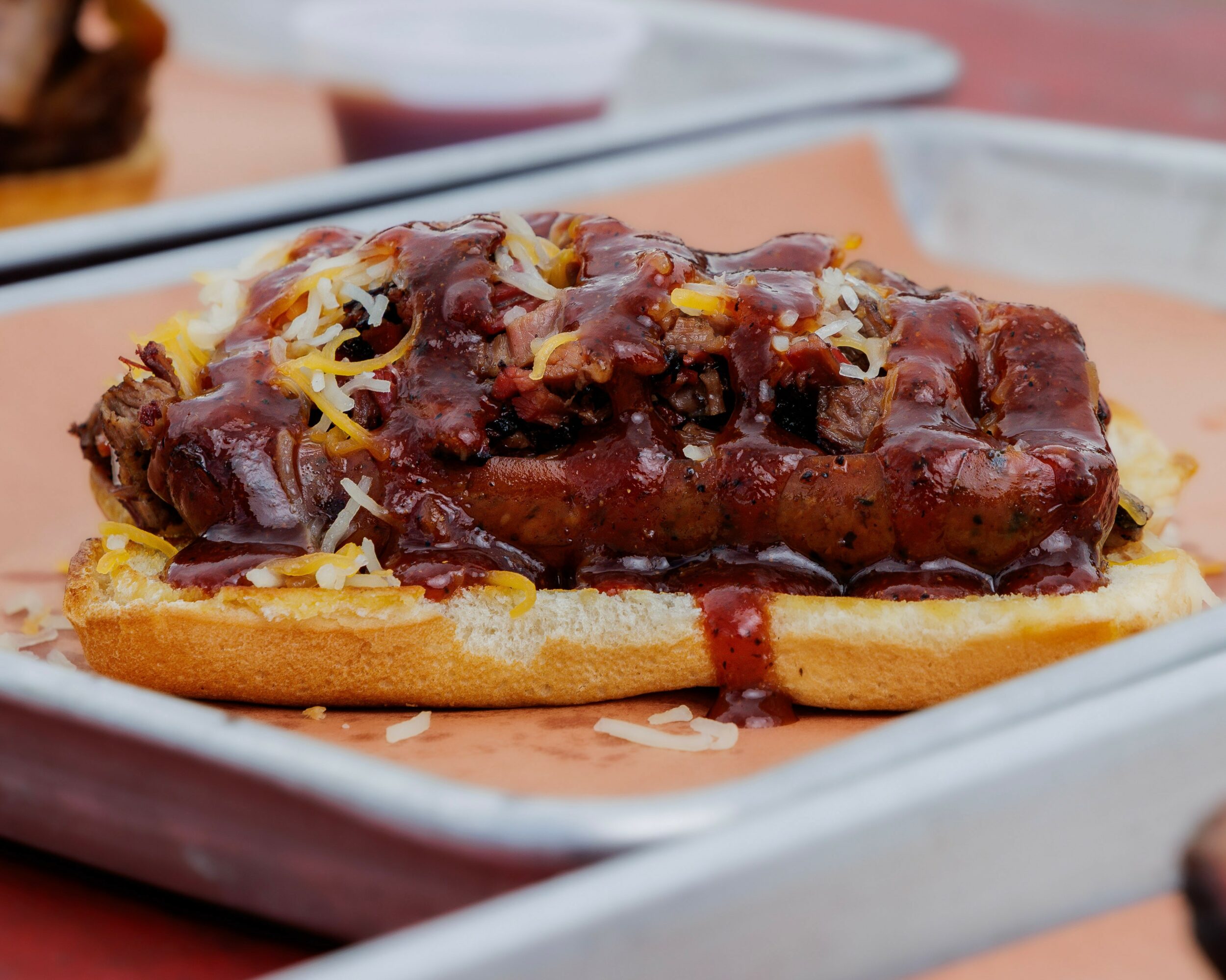 Barbecue beef sandwich with shredded cheese on a bun, served on a tray.