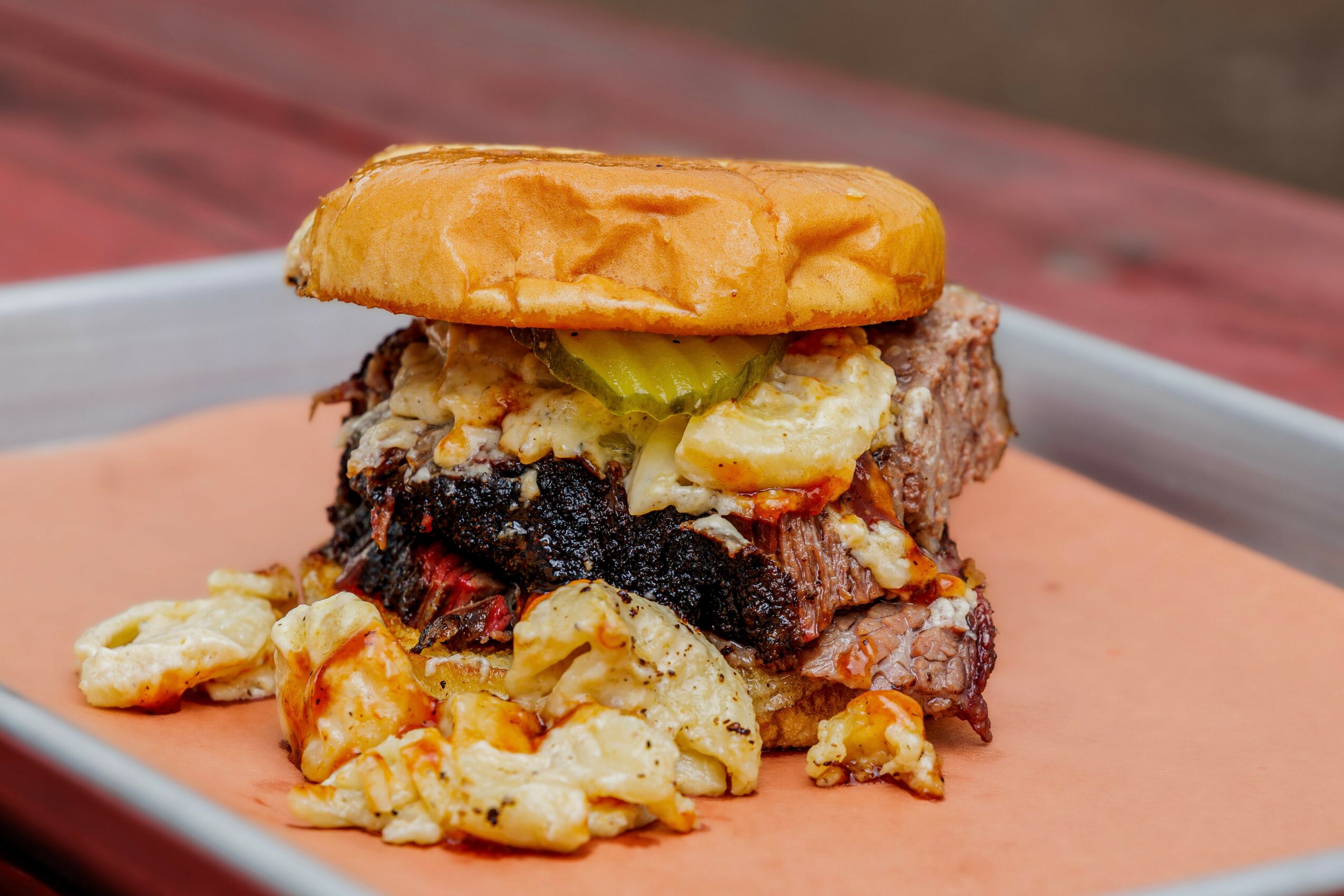A burger with a bun, a beef patty, melted cheese, lettuce, and fried onion rings on a tray.